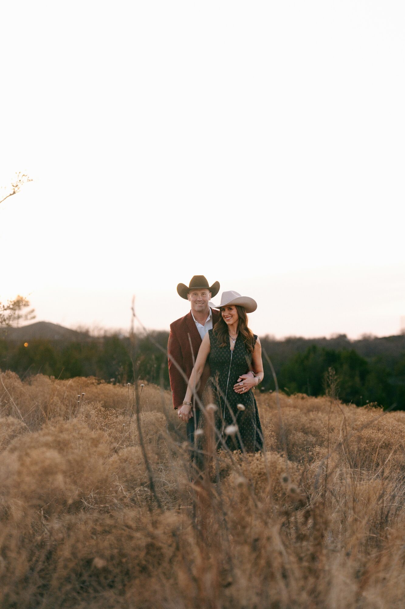 A man and woman in cowboy hats standing in a field during sunset.