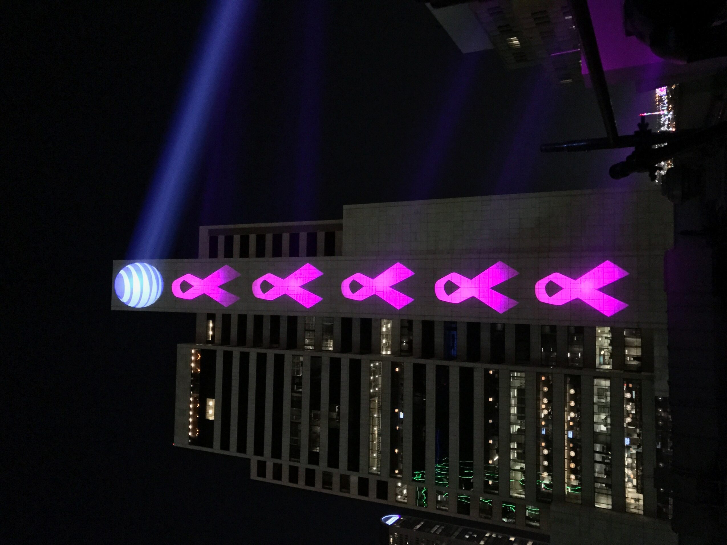 Vertical display of pink ribbons on a tall structure with city lights in the background.