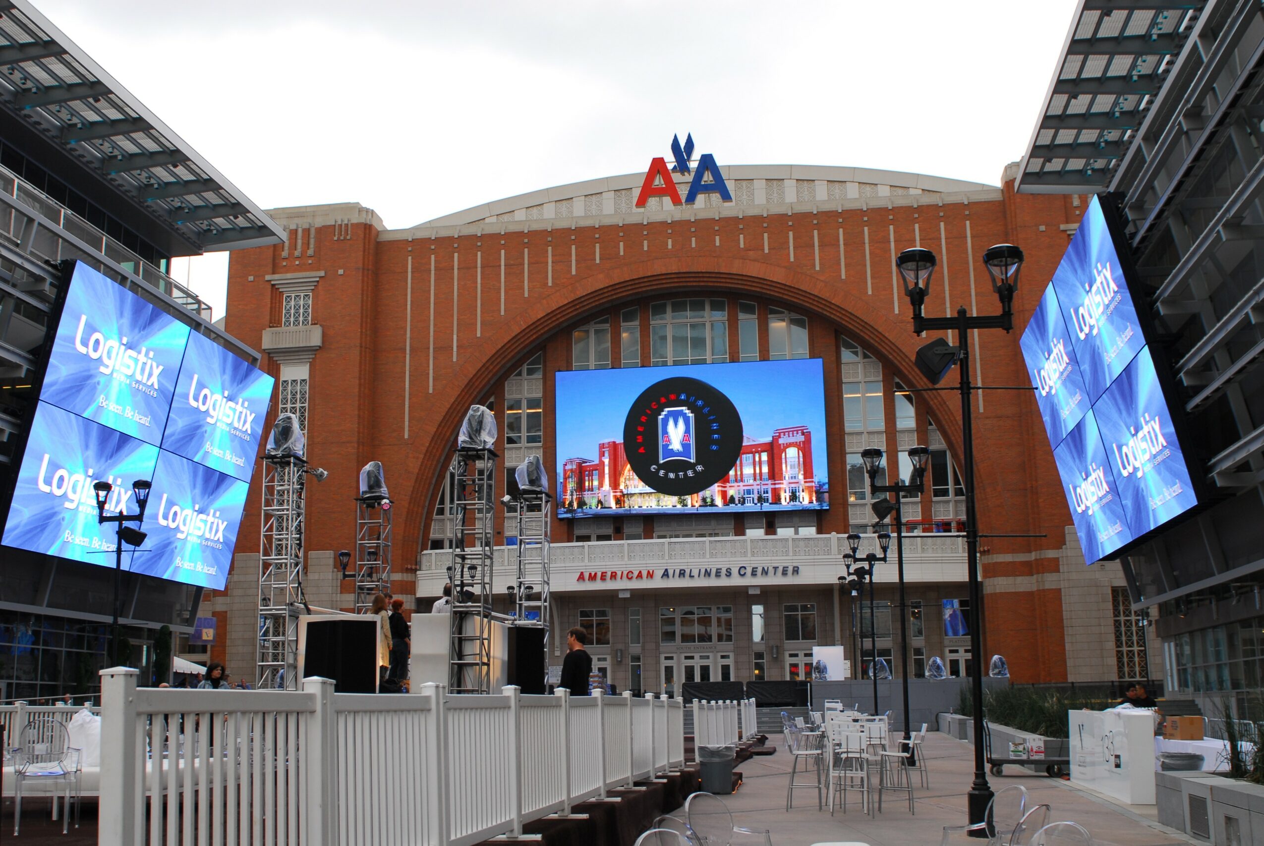 View of a large building with digital screens, a central arch, and an American Airlines sign, in an outdoor area.
