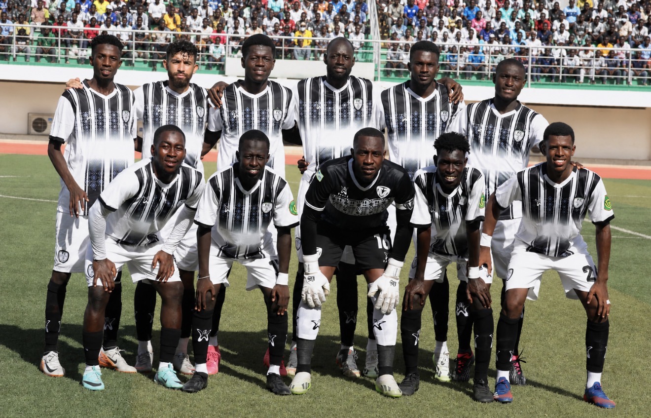 Group of ten soccer players in black and white striped uniforms on a field, with a crowd in the background.