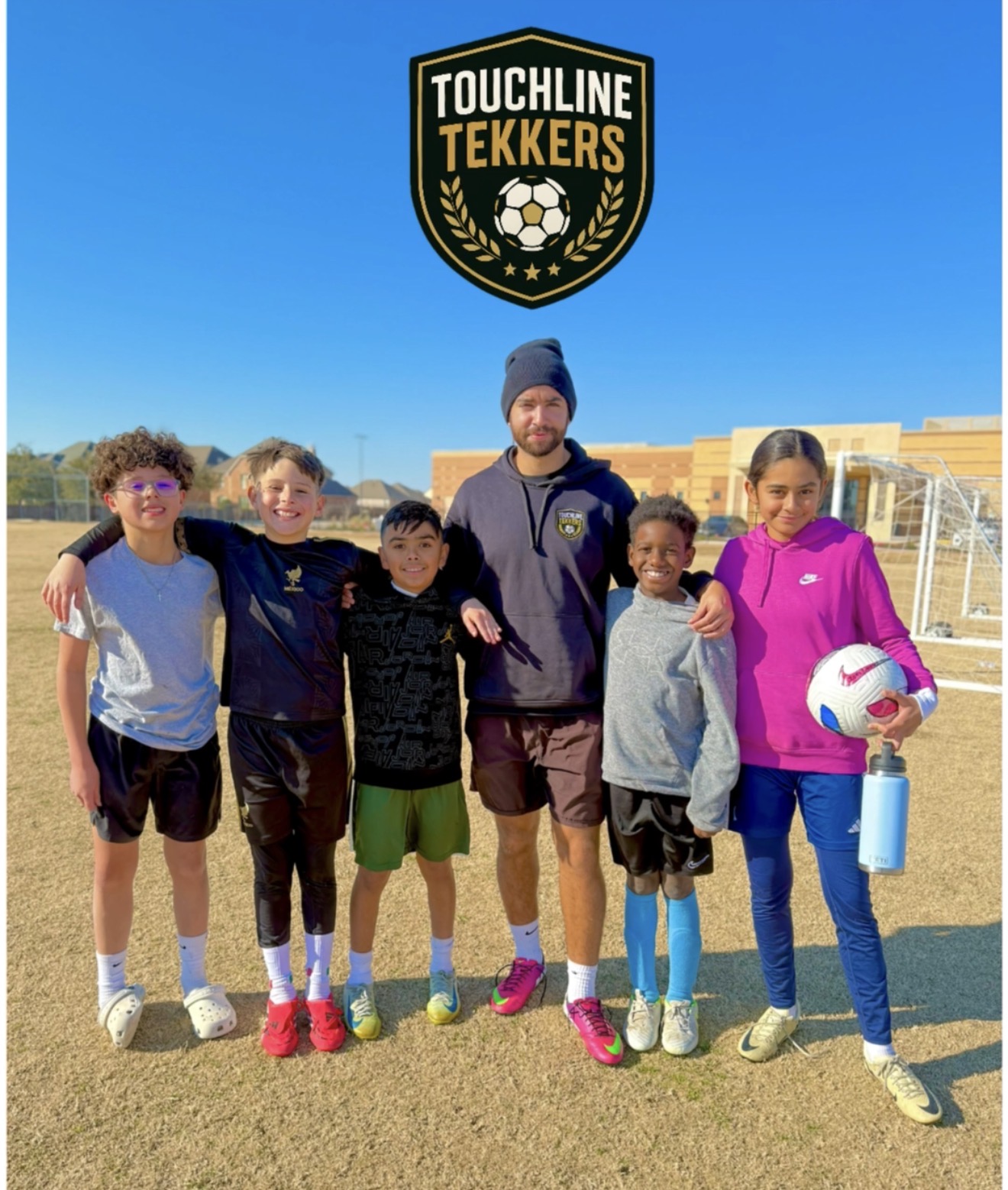 Group of children and coach standing outdoors on a sports field, with a Touchline Tekkars logo above them.