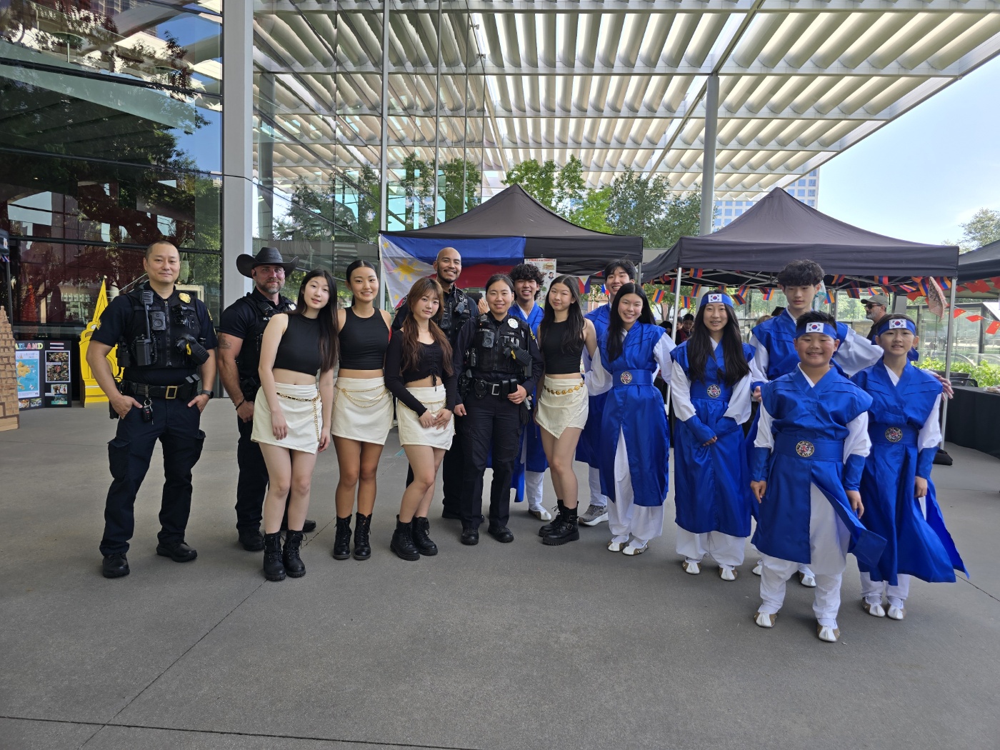 Group of people, some in police uniforms and others in traditional blue costumes, standing outside under a modern building canopy.