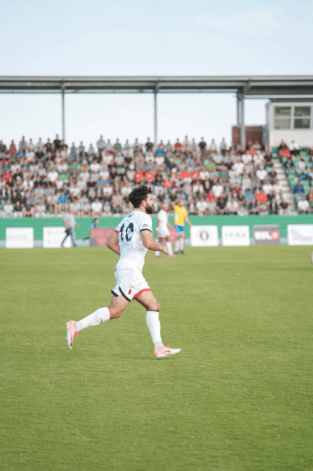 Soccer player running on field with crowd in background, wearing white uniform with number 10, green grass, stadium, sunny day