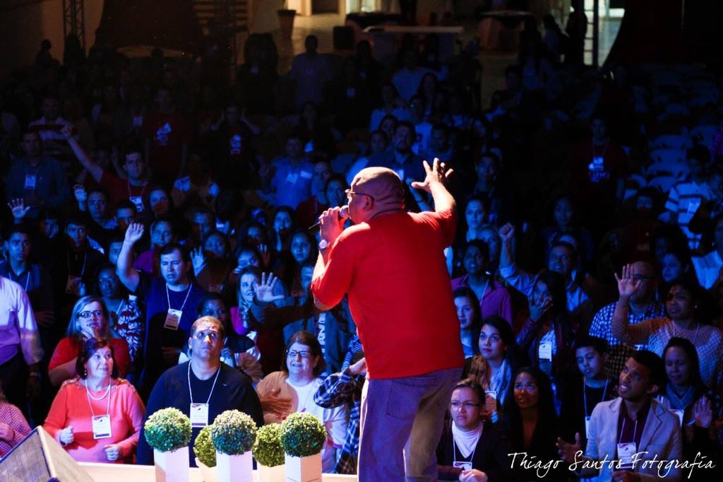 Performer on stage with a microphone in front of a large audience, stage lighting highlights the scene.