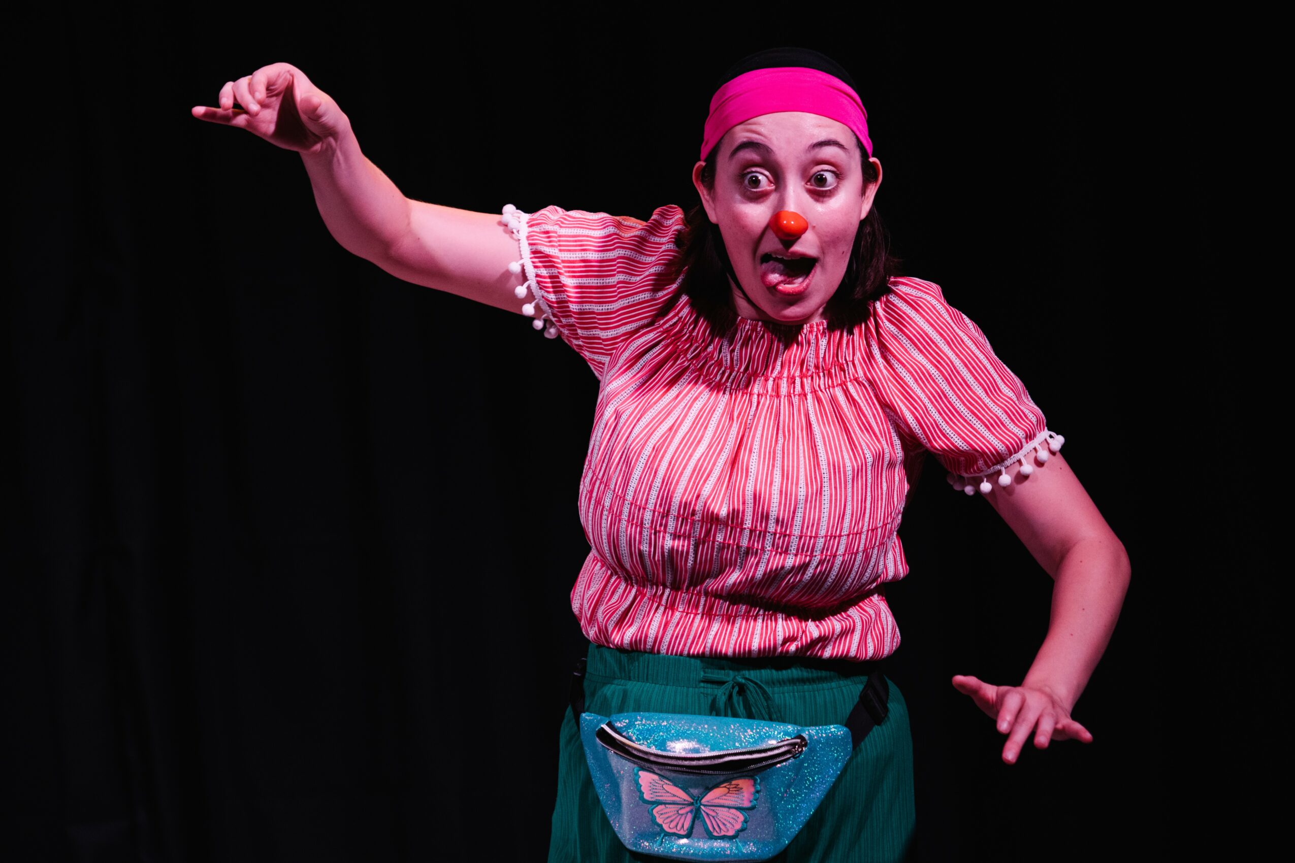 Woman in pink headscarf and striped shirt gestures with surprised expression, against a black background.
