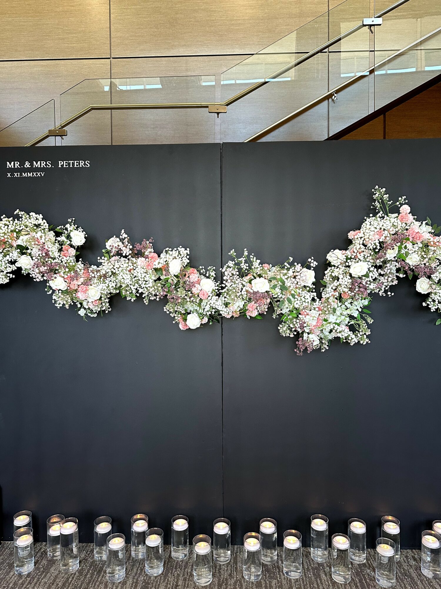 Black wall decorated with pink and white flowers, candles at the bottom, and a sign reading 'Mr. & Mrs. Peters'.
