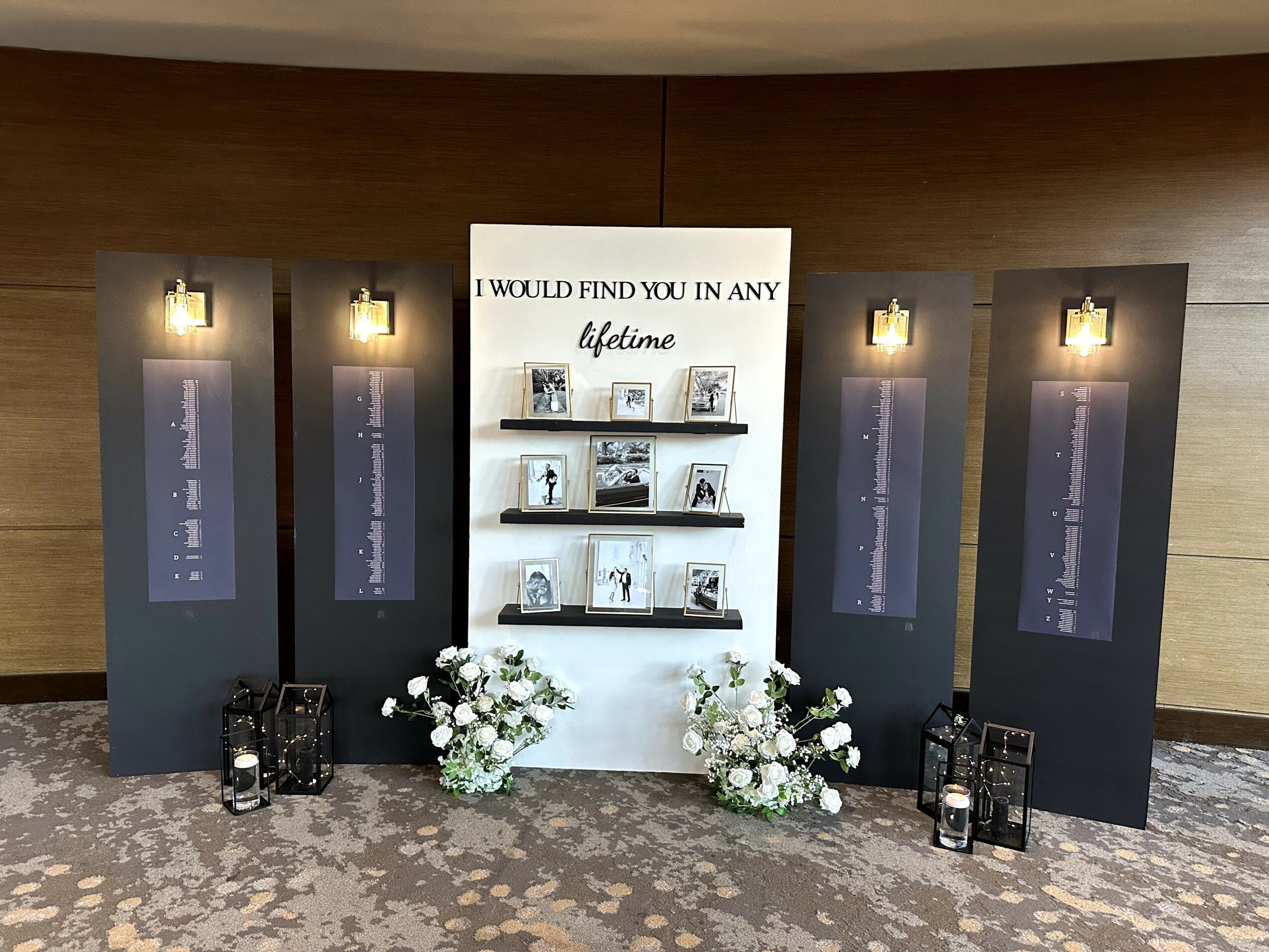 Display with four black panels, a white central shelf with books and flowers, and four lanterns on the floor.