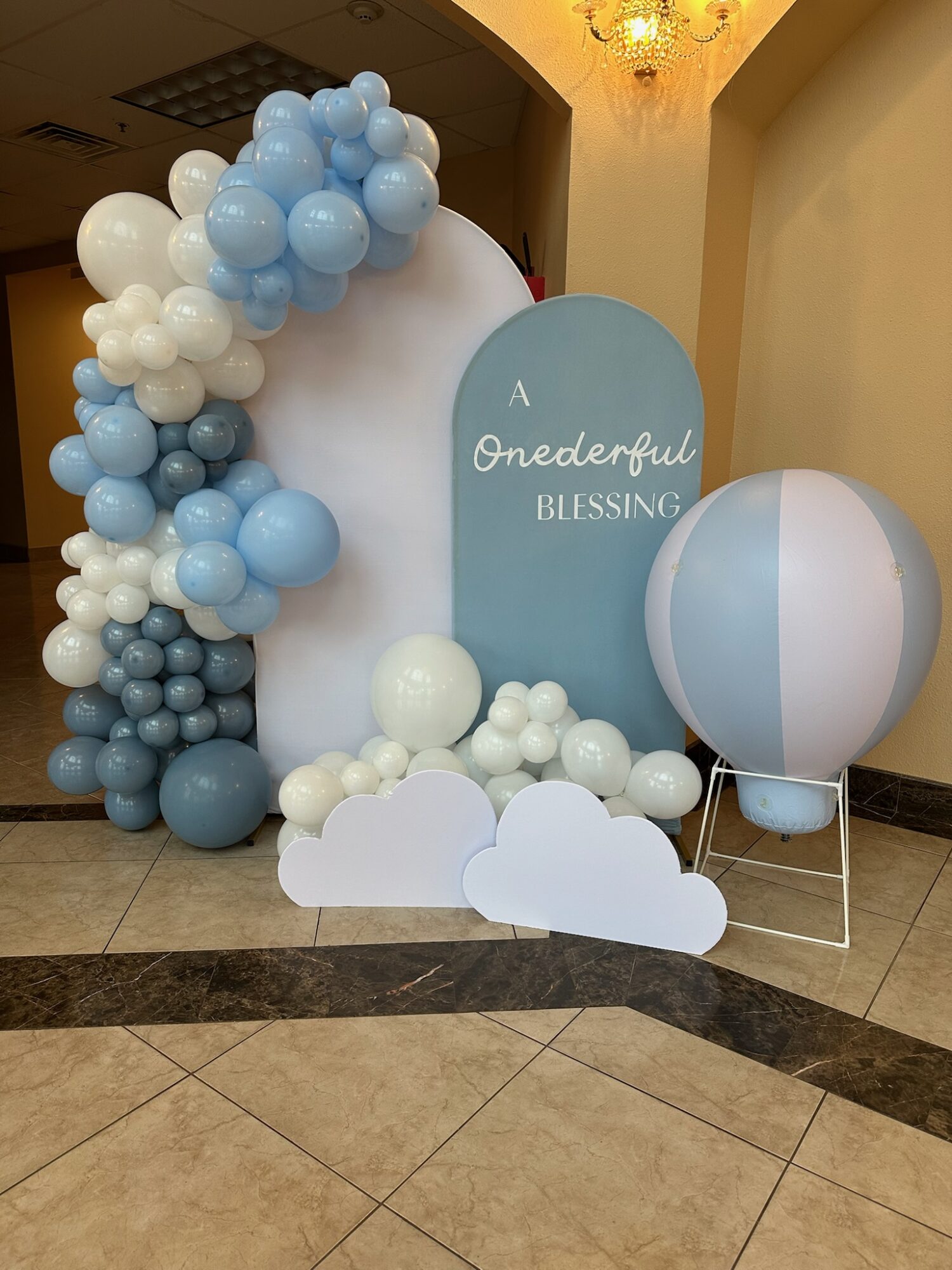 Decorative display with blue and white balloons, a large cloud, and a sign reading 'A Wonderful Blessing' in a room.