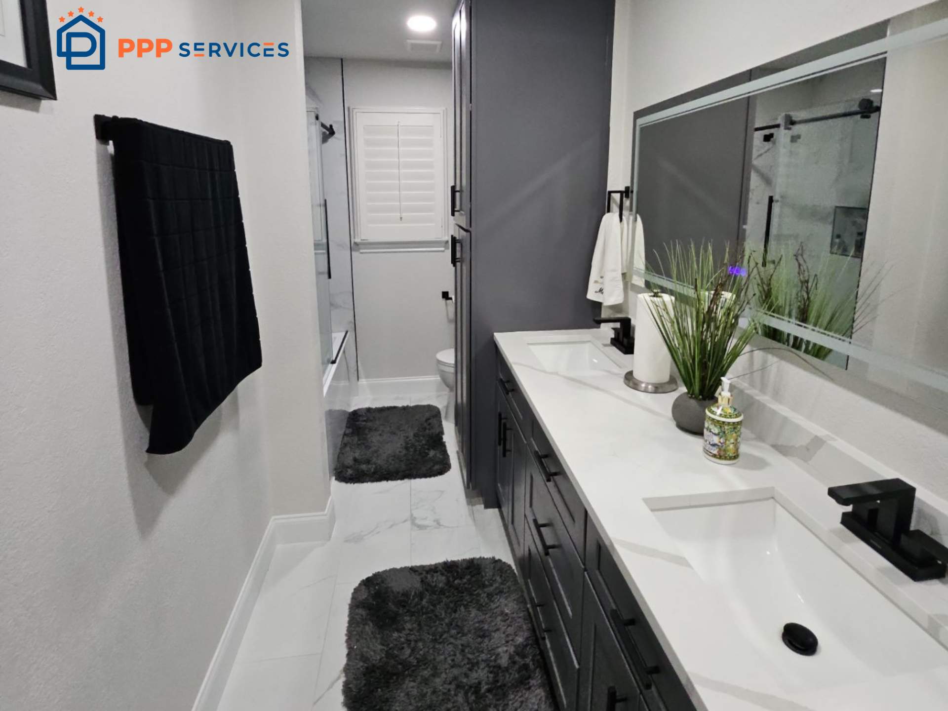 Bathroom with white walls, black towels, gray cabinets, and a white countertop with a sink, mirror, and plants.
