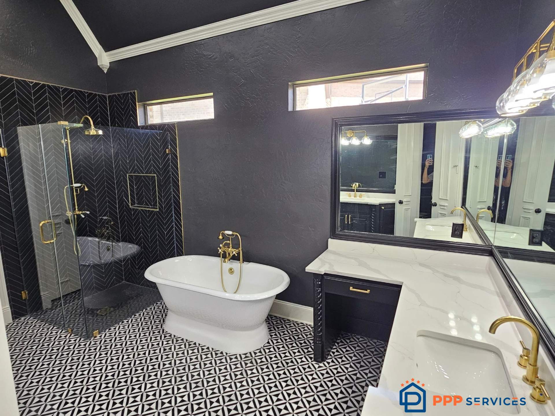 Bathroom with black walls, patterned floor, freestanding bathtub, glass shower, and white vanity with gold fixtures.