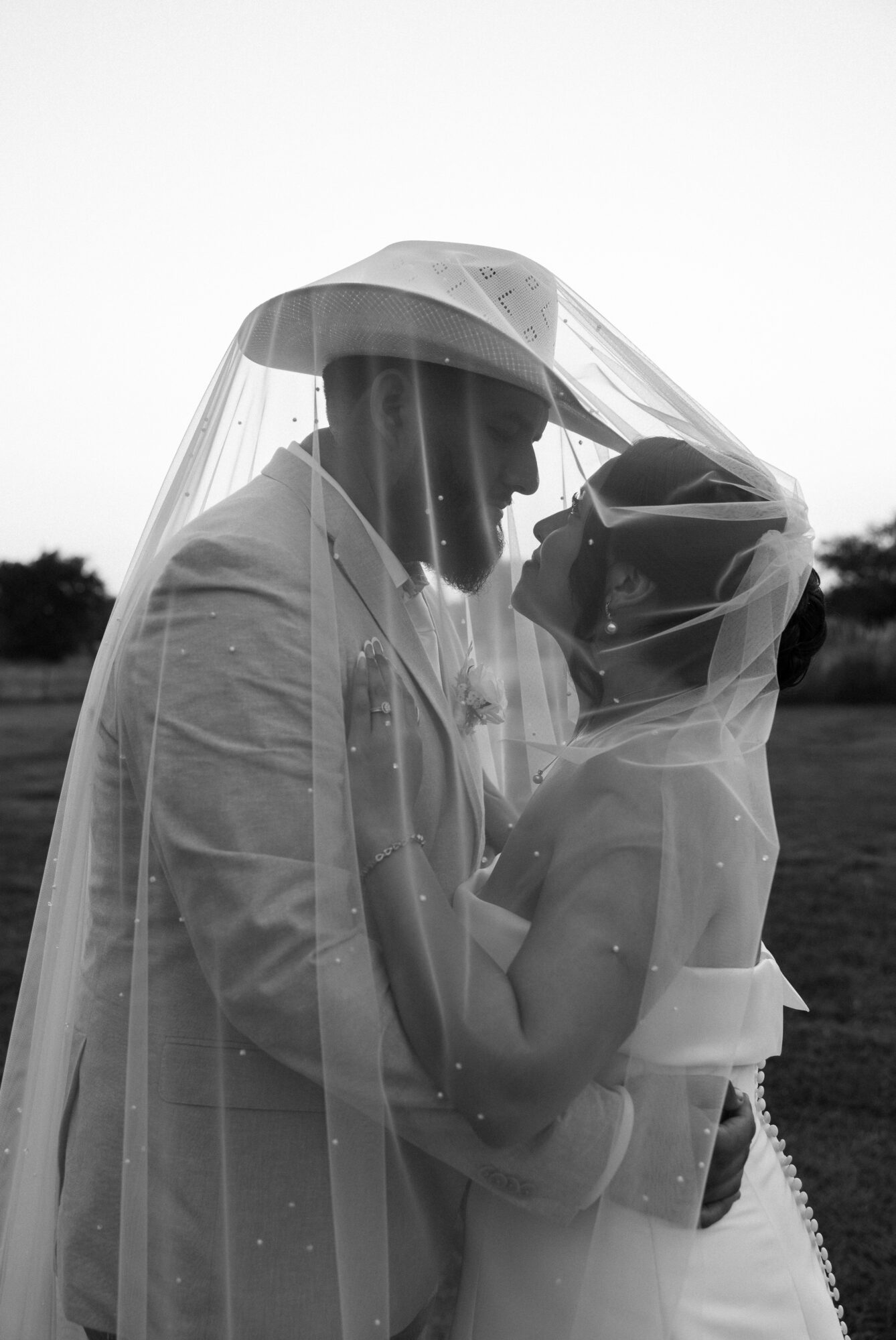 Two people under umbrellas face each other closely, with a blurred outdoor background, in black and white.
