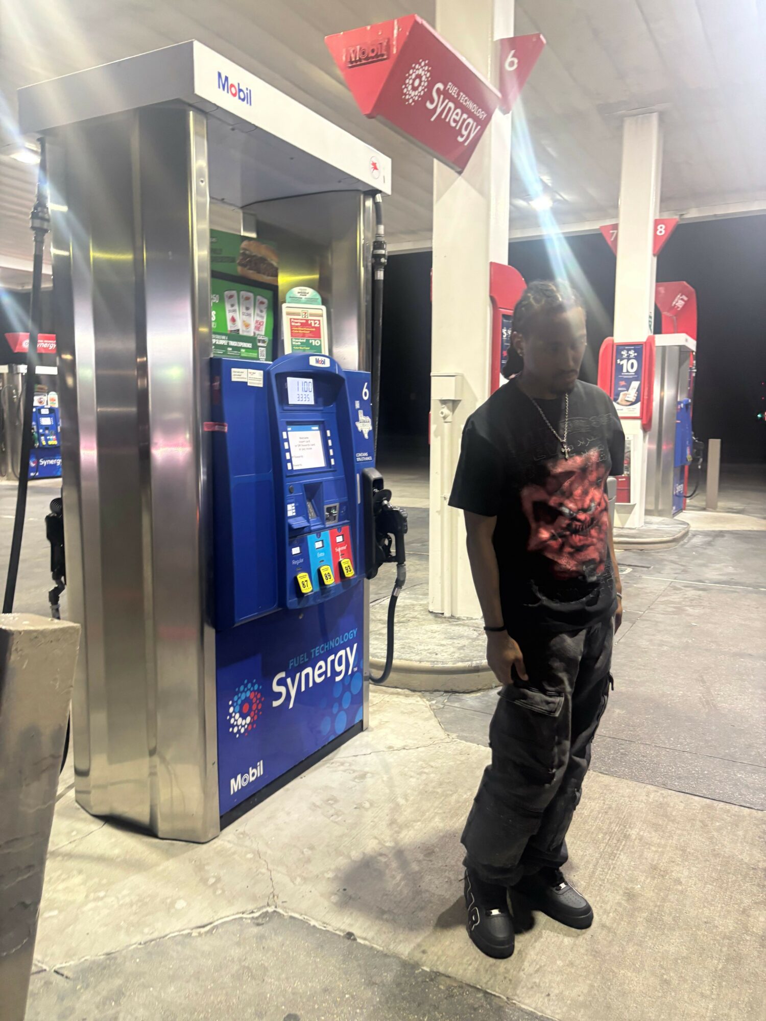 Person standing at a vending machine in a public space, with a red sign above and a gray floor.