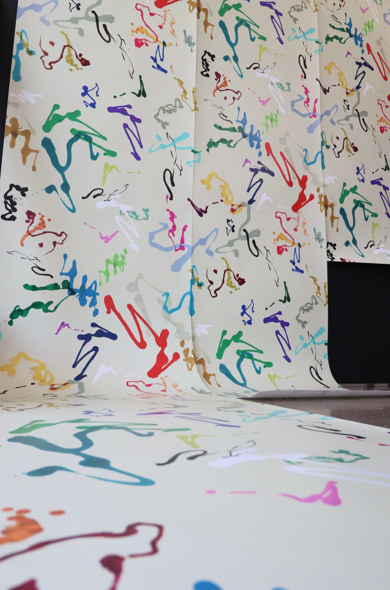 Colorful abstract squiggles on a white background, with part of a black object visible in the lower right corner.