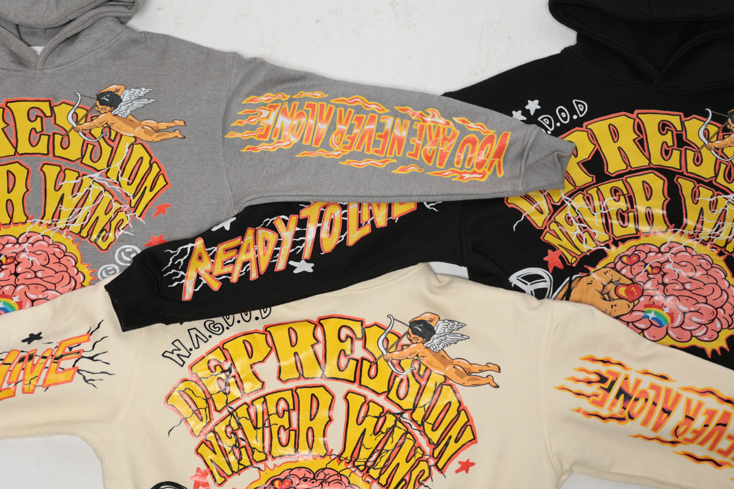 Multiple colorful T-shirts with graphic designs and text, overlapping each other, in various colors including yellow, black, and white.