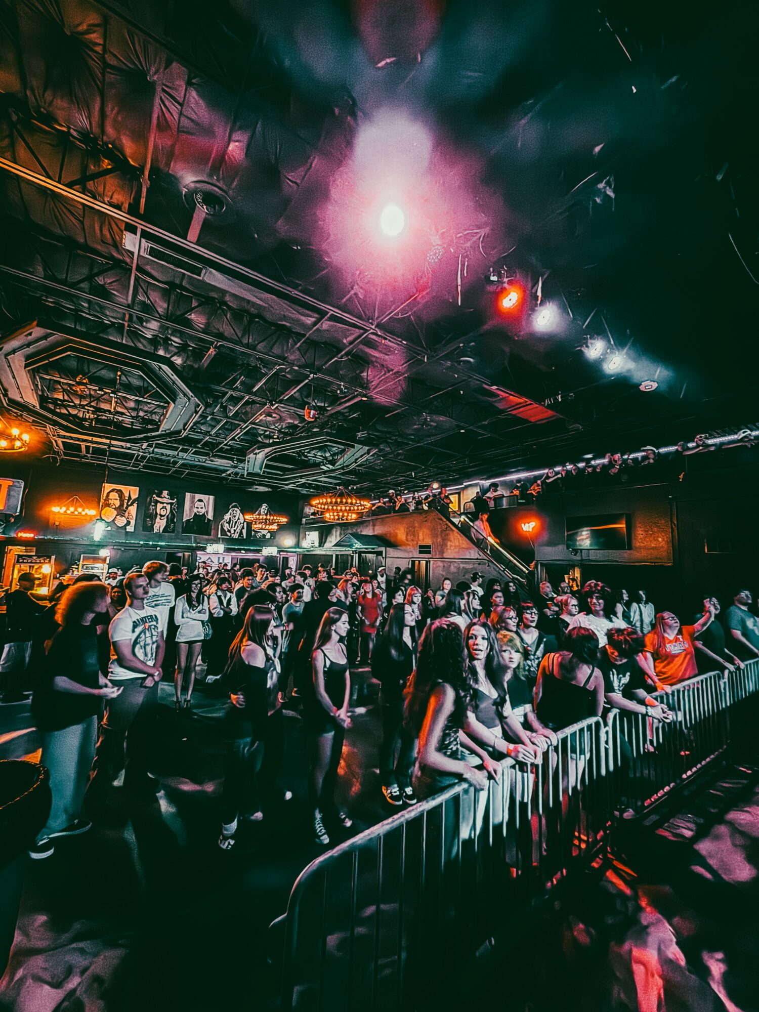 Crowd of people at a concert or event with stage lighting and a dark indoor setting.