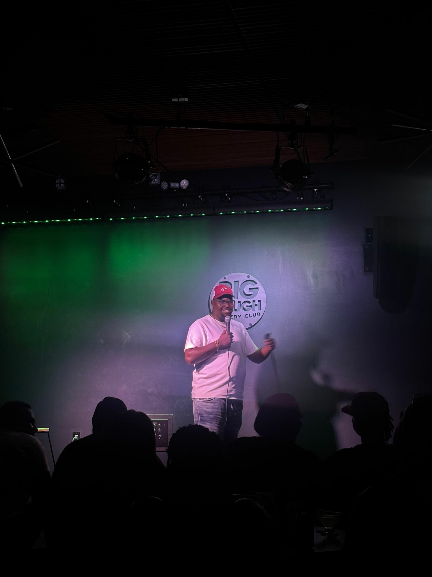 Performer on stage with microphone, colorful lighting, audience silhouettes, fog effects, and a clock backdrop.