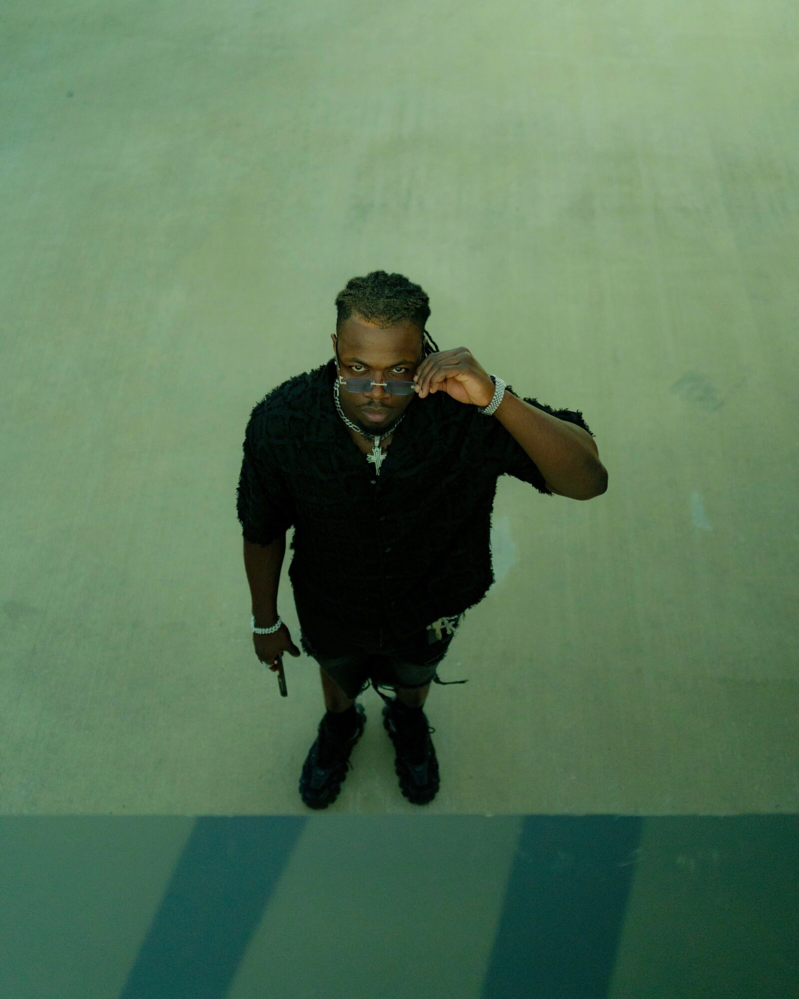 Person with glasses and braided hair taking a selfie from above, standing on a greenish floor.