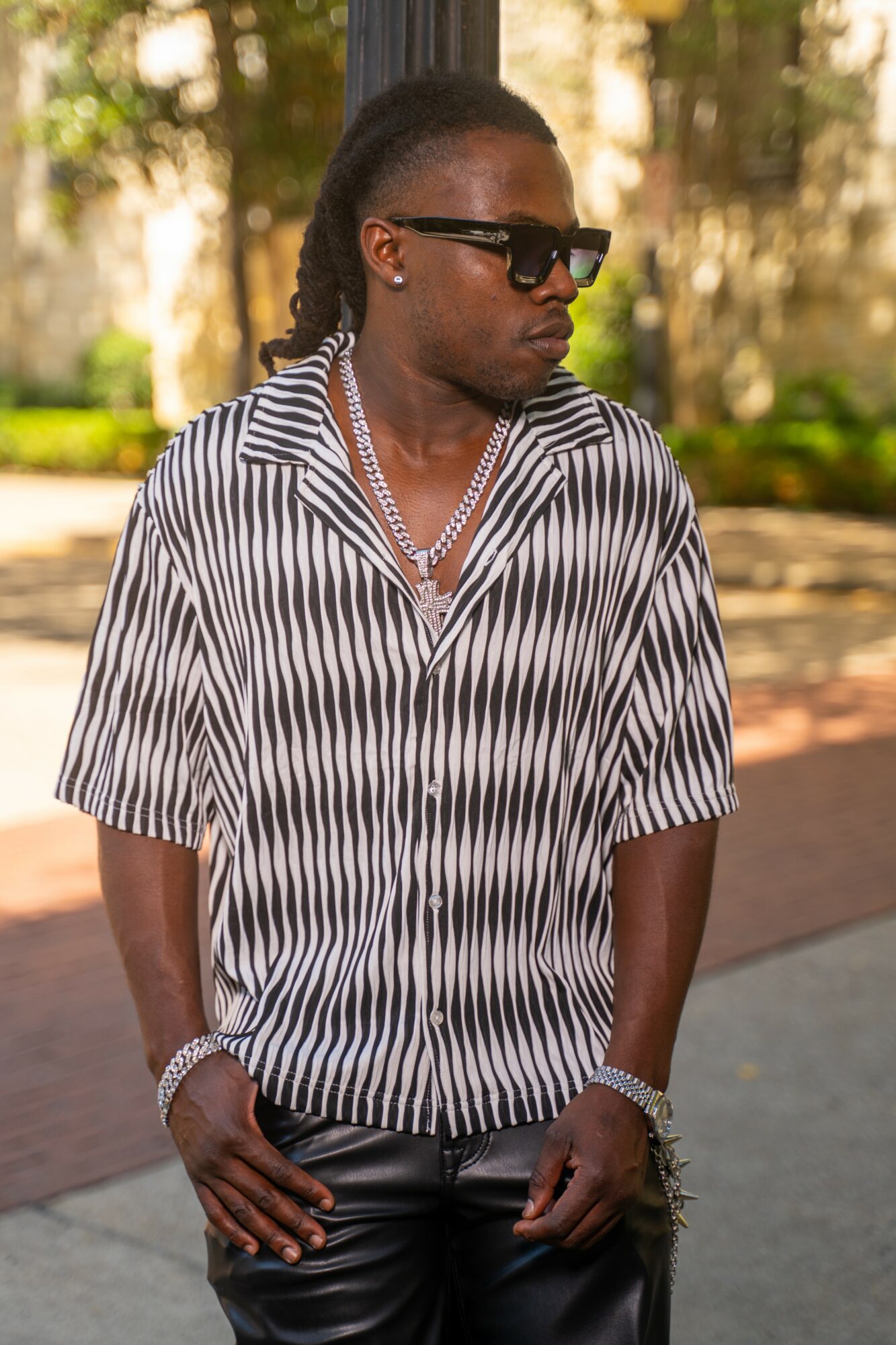 Woman with sunglasses, striped shirt, and jewelry outdoors, standing with hands in pockets.