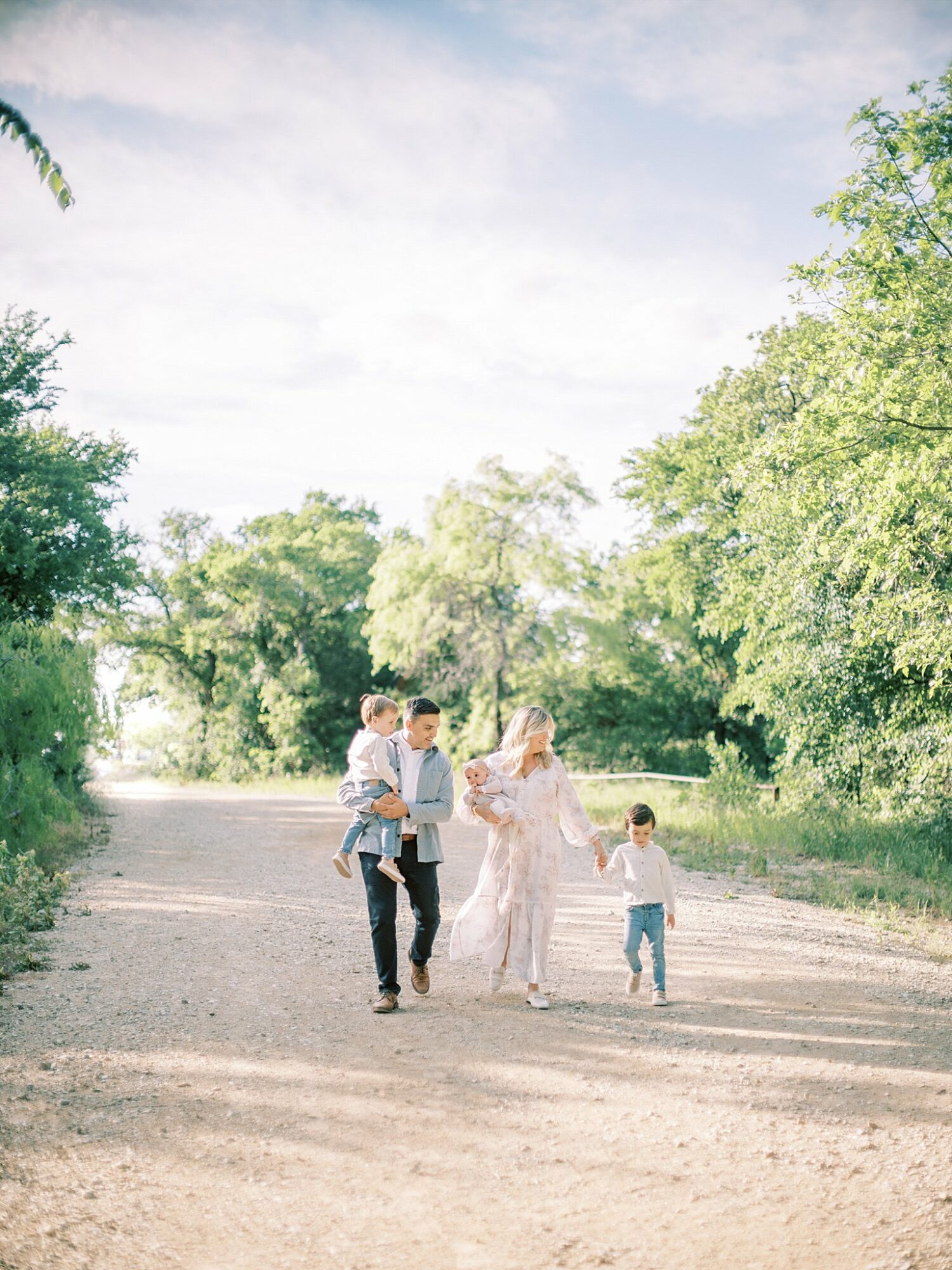 Group of five people walking on a dirt path surrounded by trees and greenery, under a partly cloudy sky.