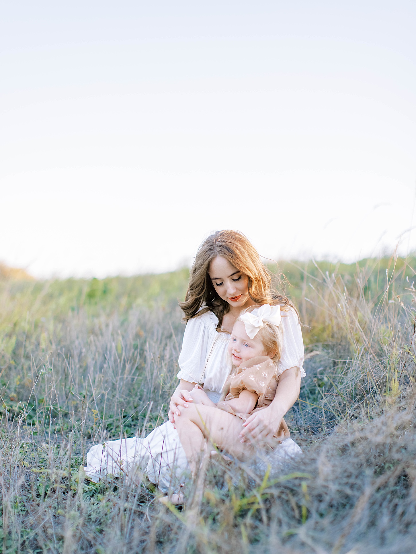 Two children sitting in a grassy field, one with long hair and the other with short hair, embracing each other.