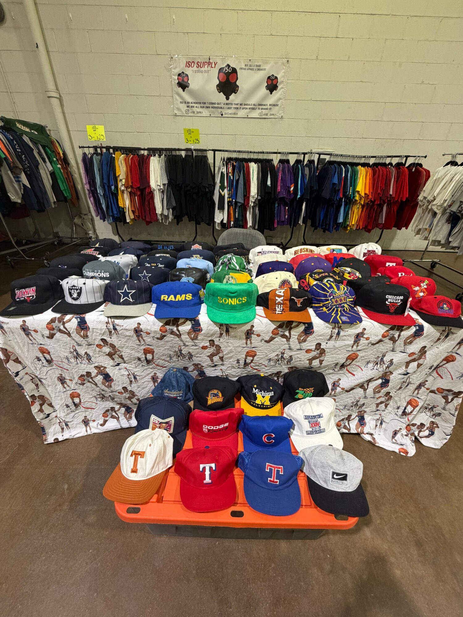 Display of colorful clothing, hats, and accessories on a table and rack in a store, with a yellow wall in the background.