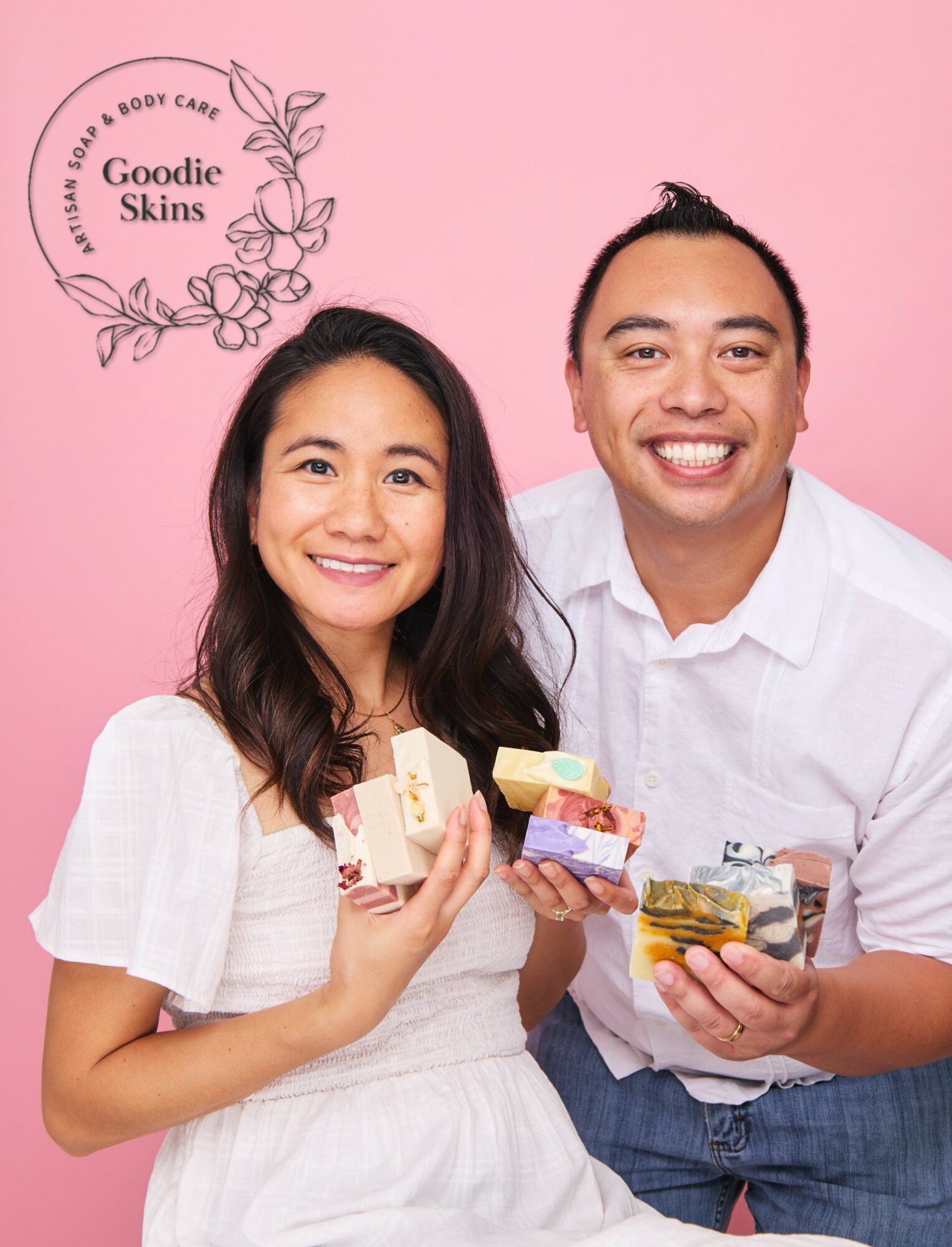 Two smiling people holding small gift boxes against a pink background, with a logo reading 'Goodie Skins' in the top left corner.