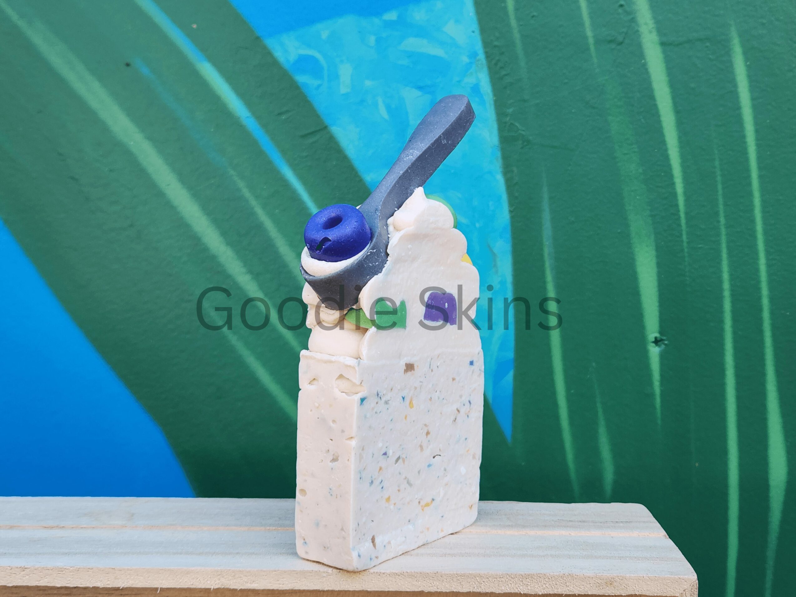 A popsicle with a blue and white handle, partially eaten, on a wooden surface with green and blue background.