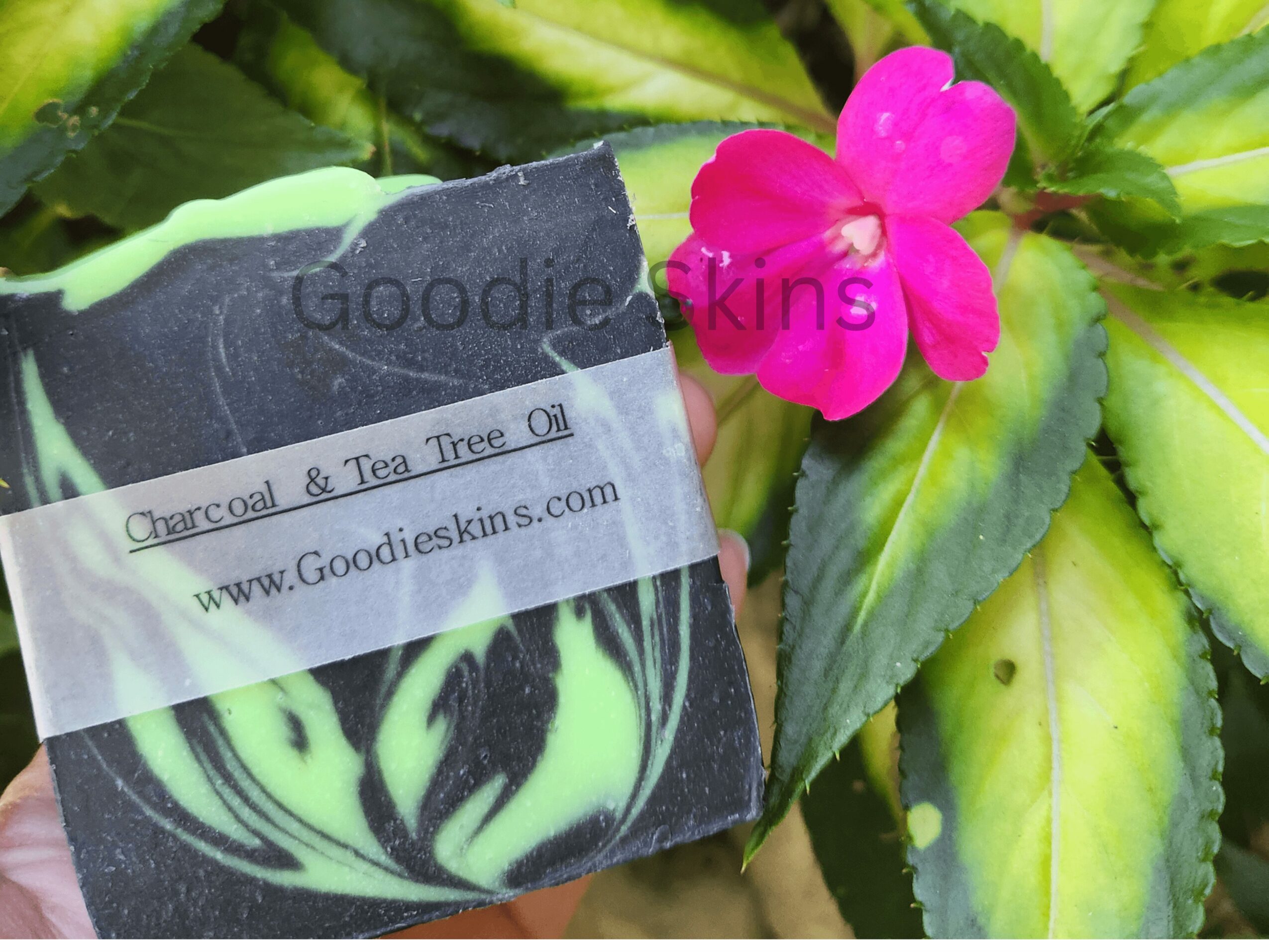 Pink flower with green leaves, and a black and green soap bar with label, outdoors.
