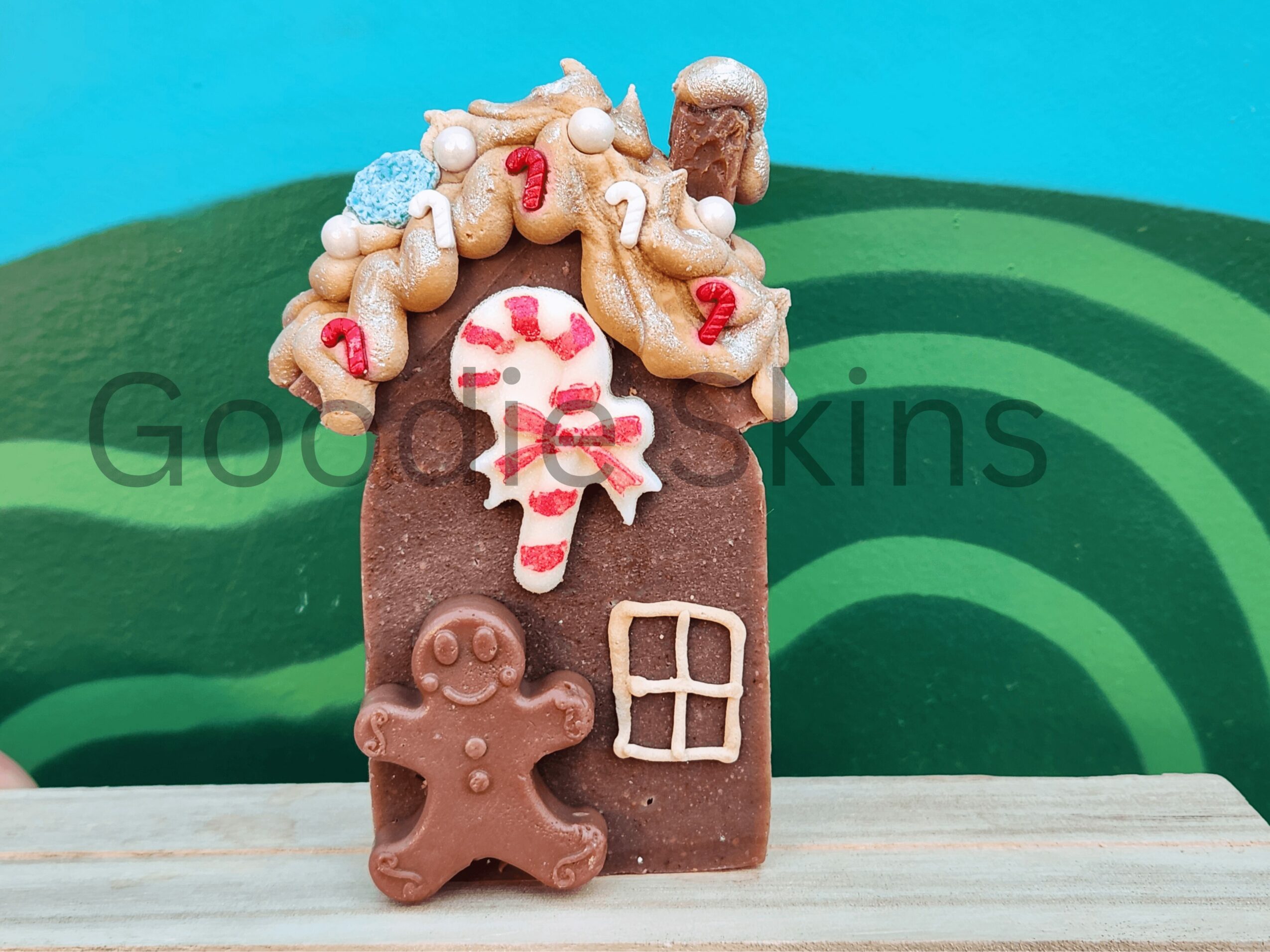 Gingerbread house decorated with candies, a gingerbread person, and a window, set against a green and blue background.