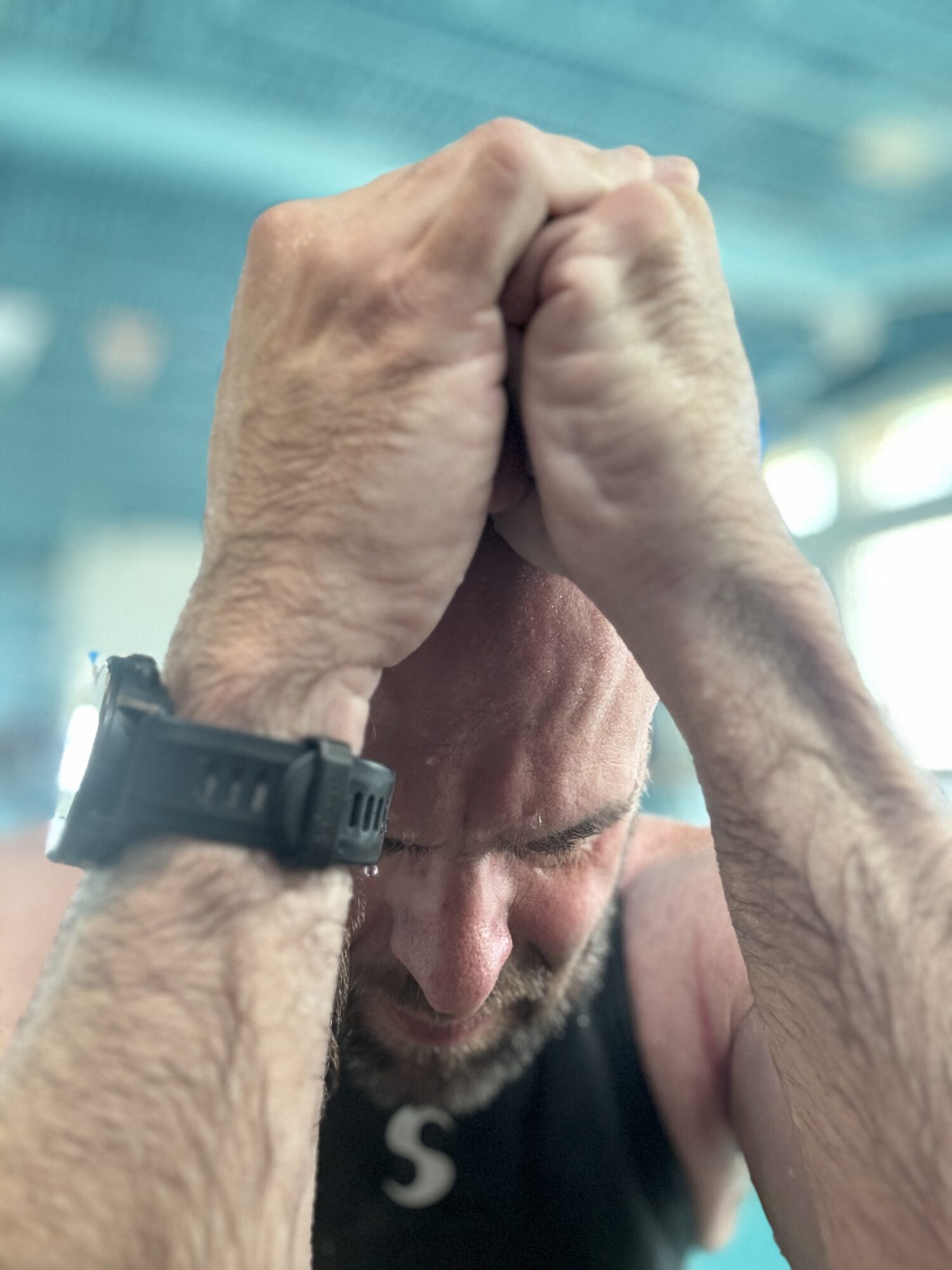 Person with hands clasped on head, eyes closed, wearing a watch, in a sports setting.