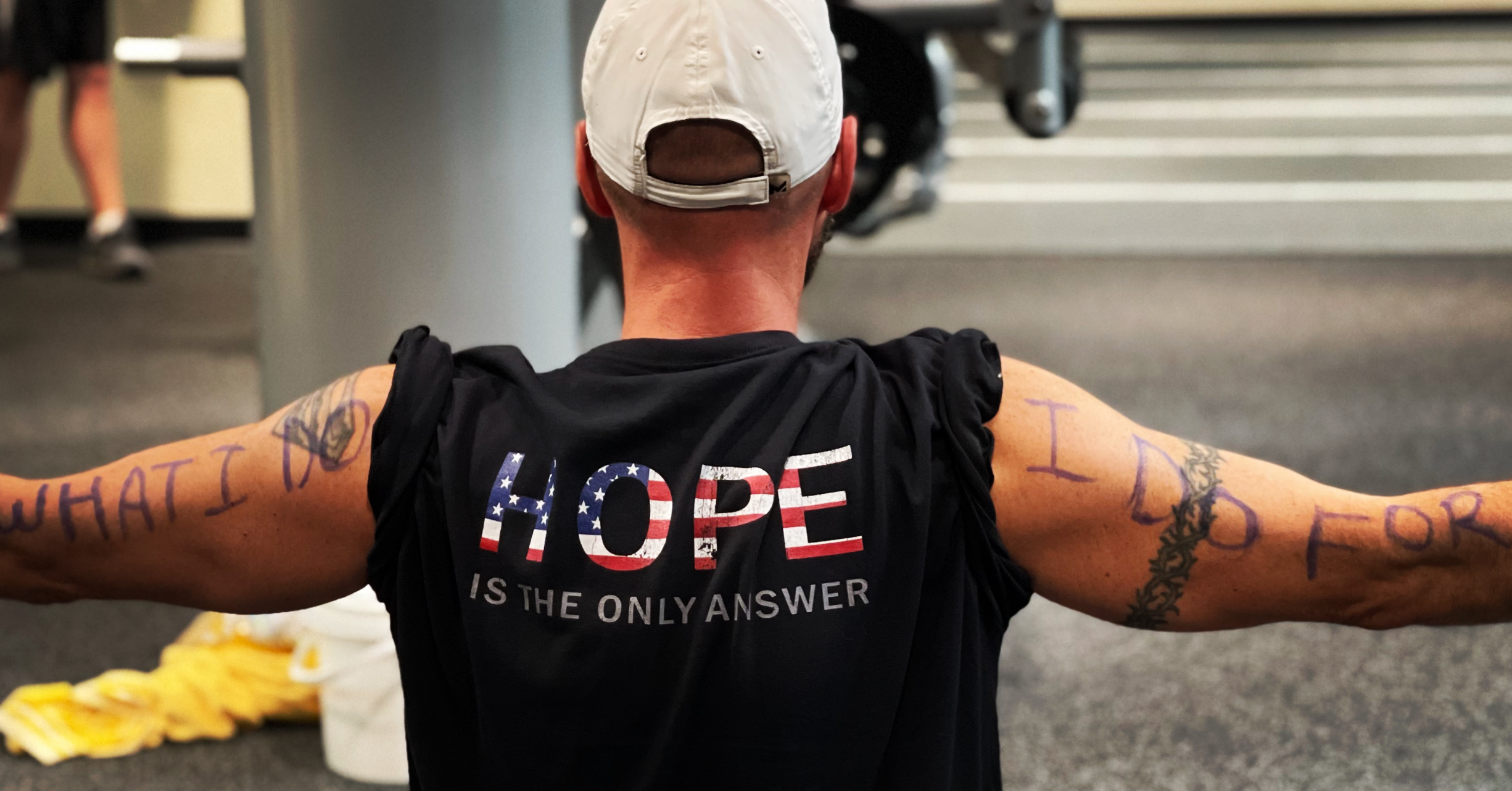 Person with arms outstretched, wearing a black shirt with 'HOPE' written on back, in a public space.