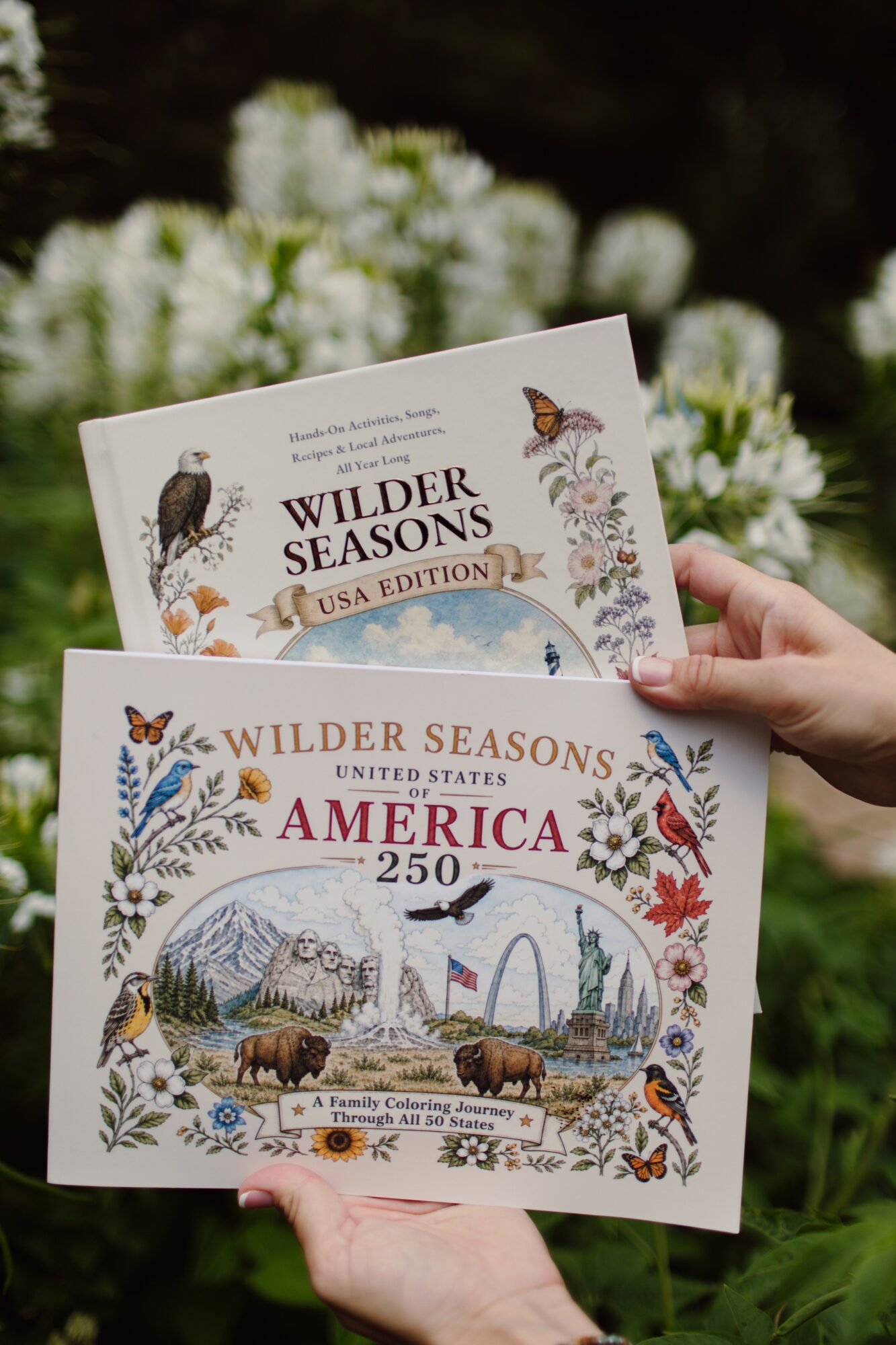 Person holding two illustrated books about America and wildlife, with a blurred garden background.