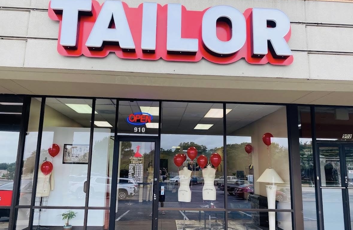 Storefront with large pink and white sign reading 'TAILOR' and window display with red balloons and mannequins.