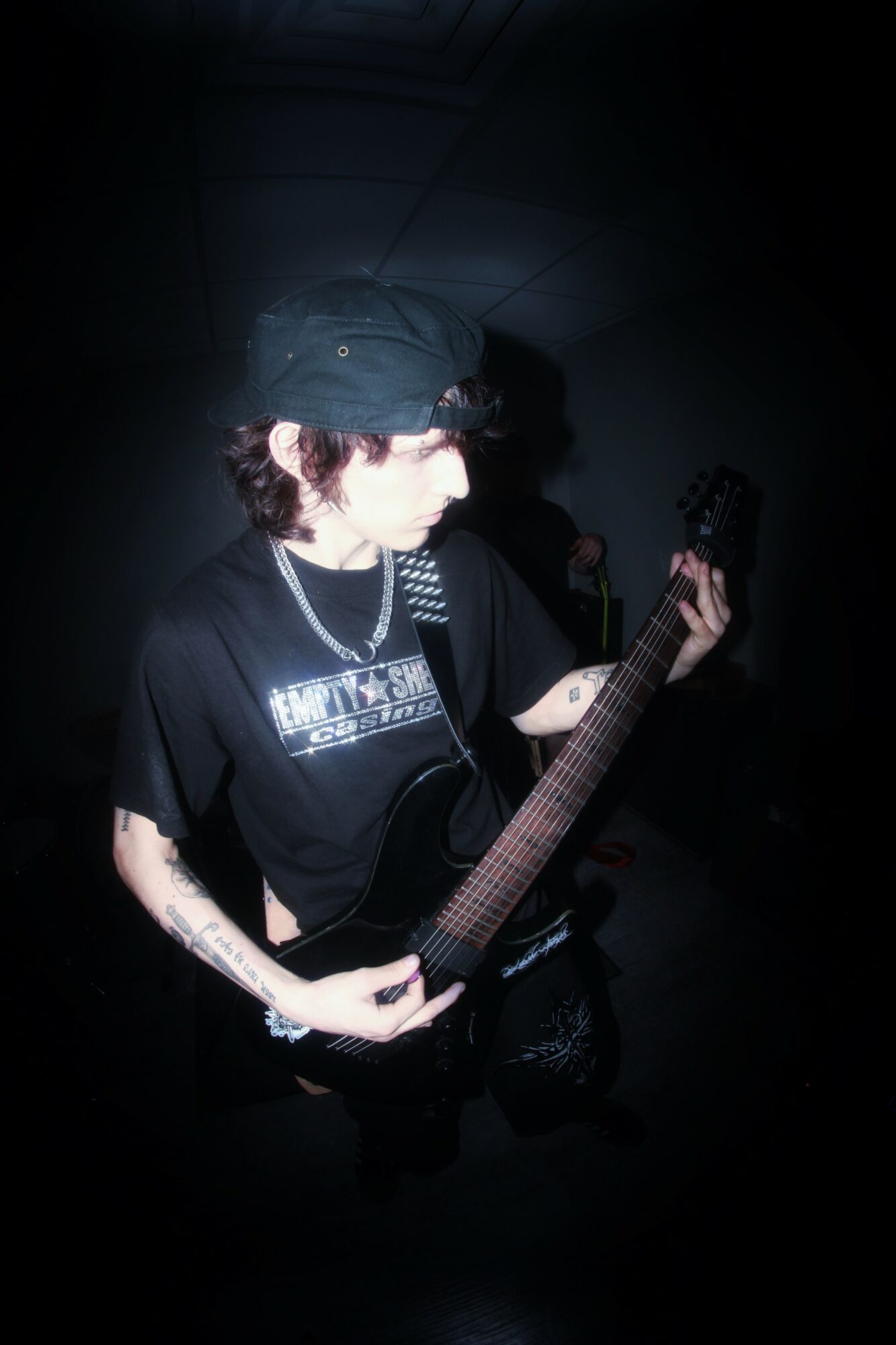 Person wearing a hat and sunglasses playing an electric guitar in a dark setting.