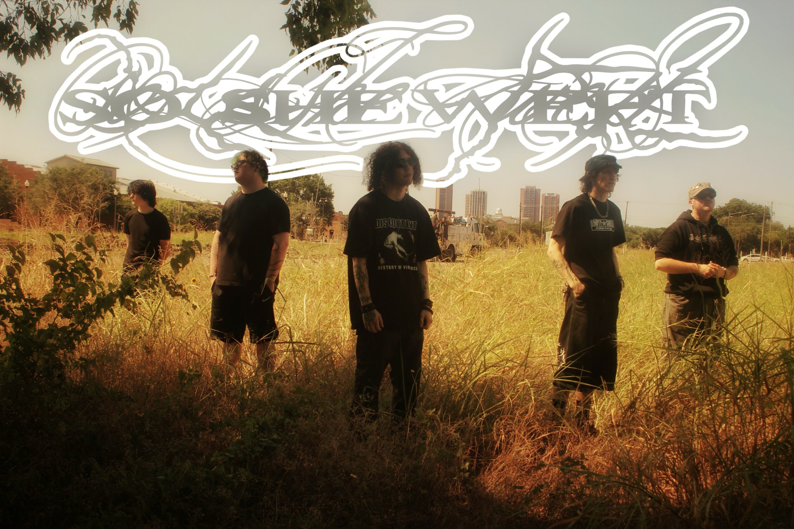 Five people standing in a grassy field with a city skyline in the background, some holding objects, under a cloudy sky.