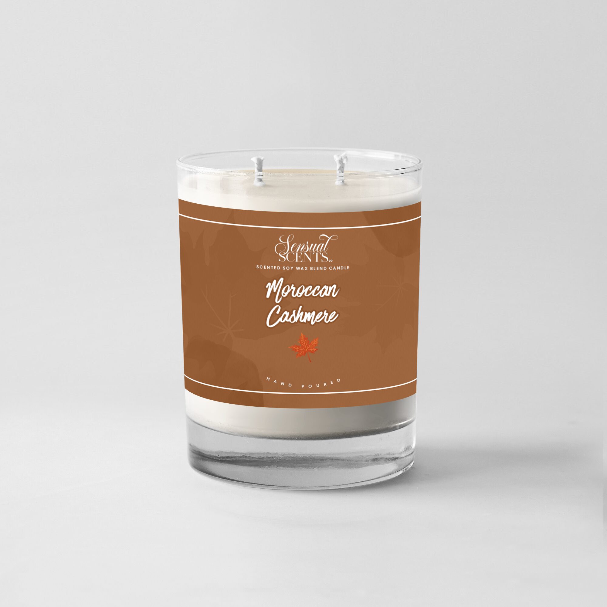 A candle in a glass container with a brown label reading Moroccan Cashmere, two wicks, and a white wax base.