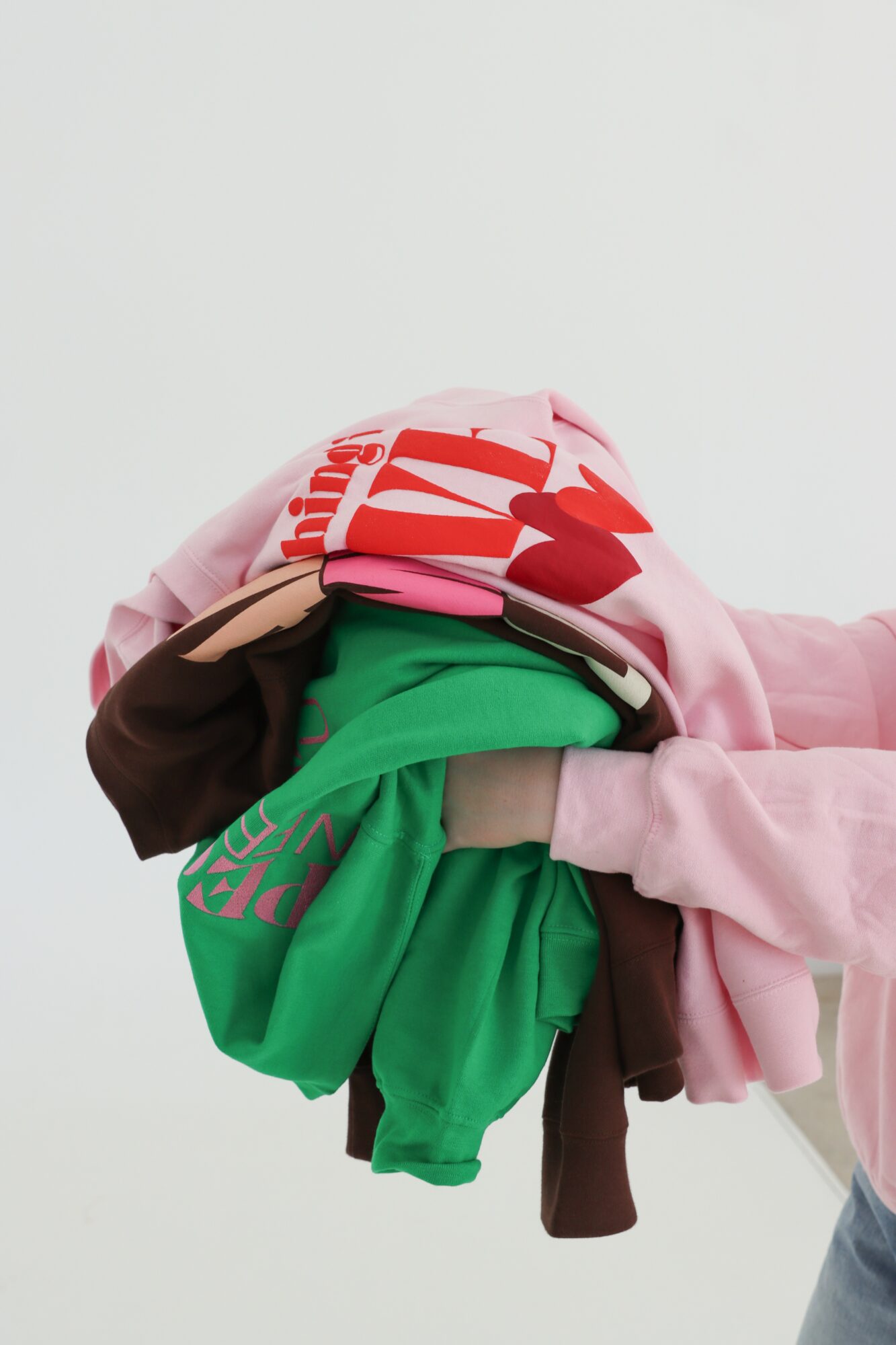 Person holding a pile of colorful folded clothes against a plain background.