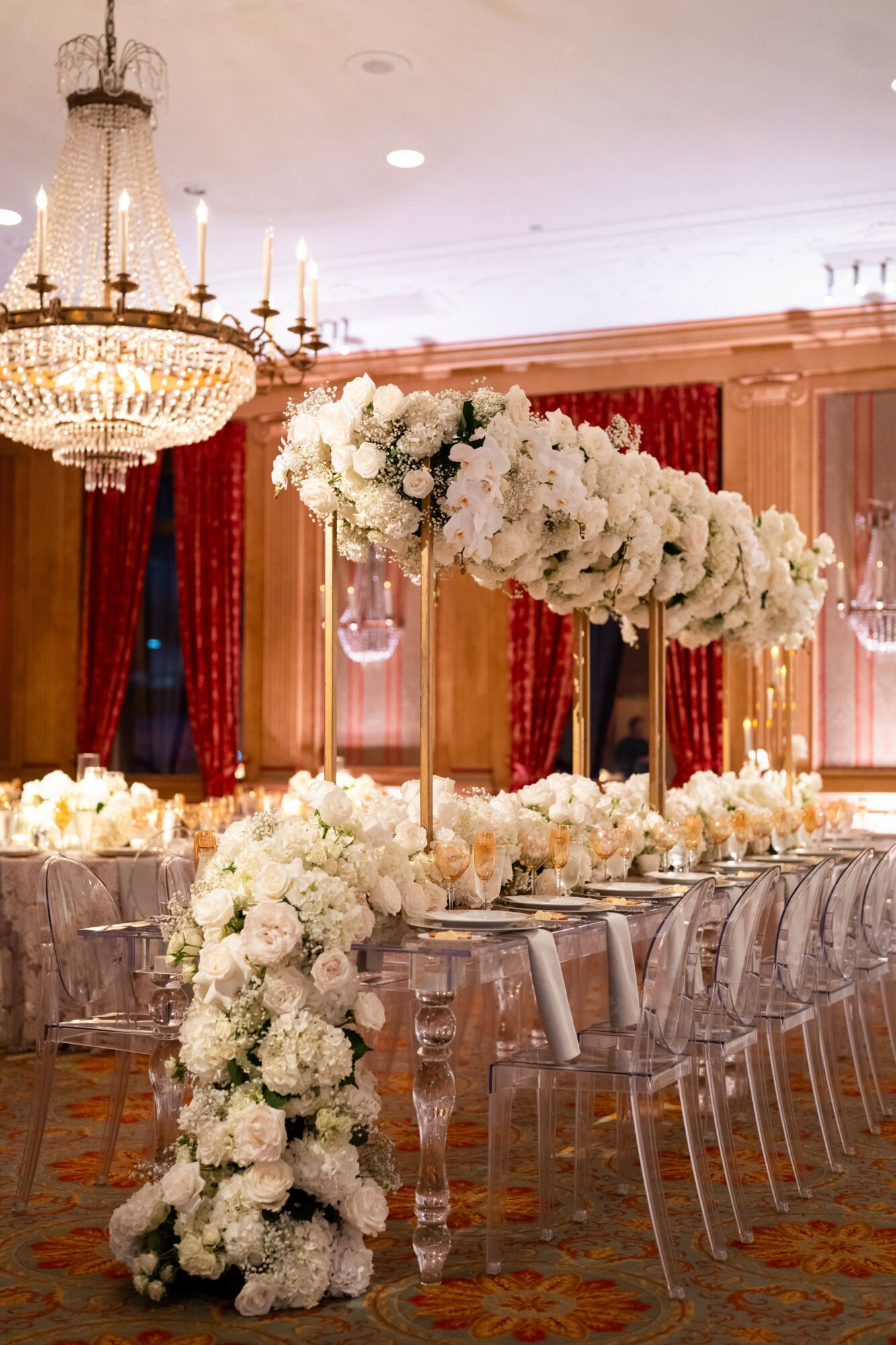 Elegant event space with a large floral centerpiece, chandelier, and red curtains, set for a formal gathering.