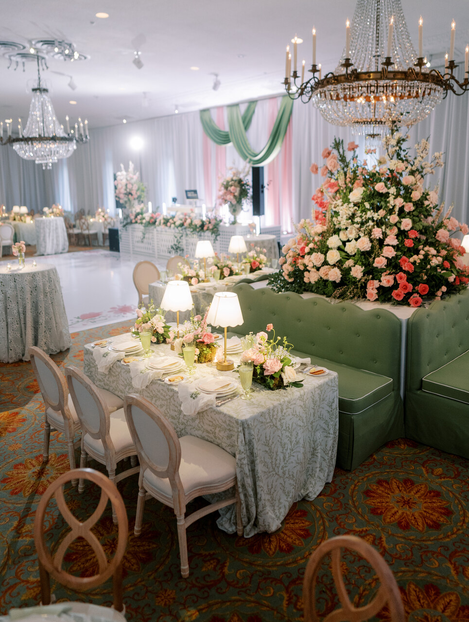 Elegant event space with chandeliers, floral arrangements, and decorated tables, featuring a large floral centerpiece and draped fabric.
