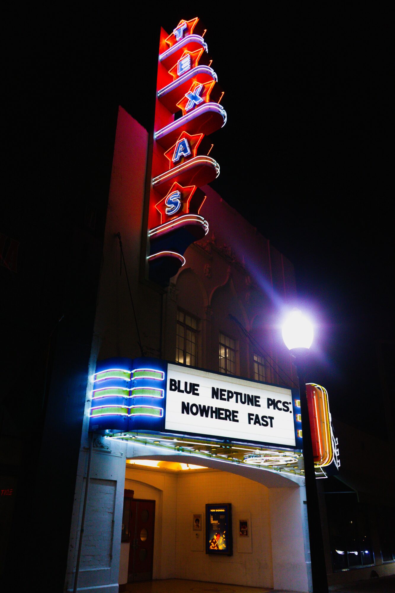 Vertical neon sign with the word 'PEARL' and a marquee displaying a quote about Neptune pictures, at night.