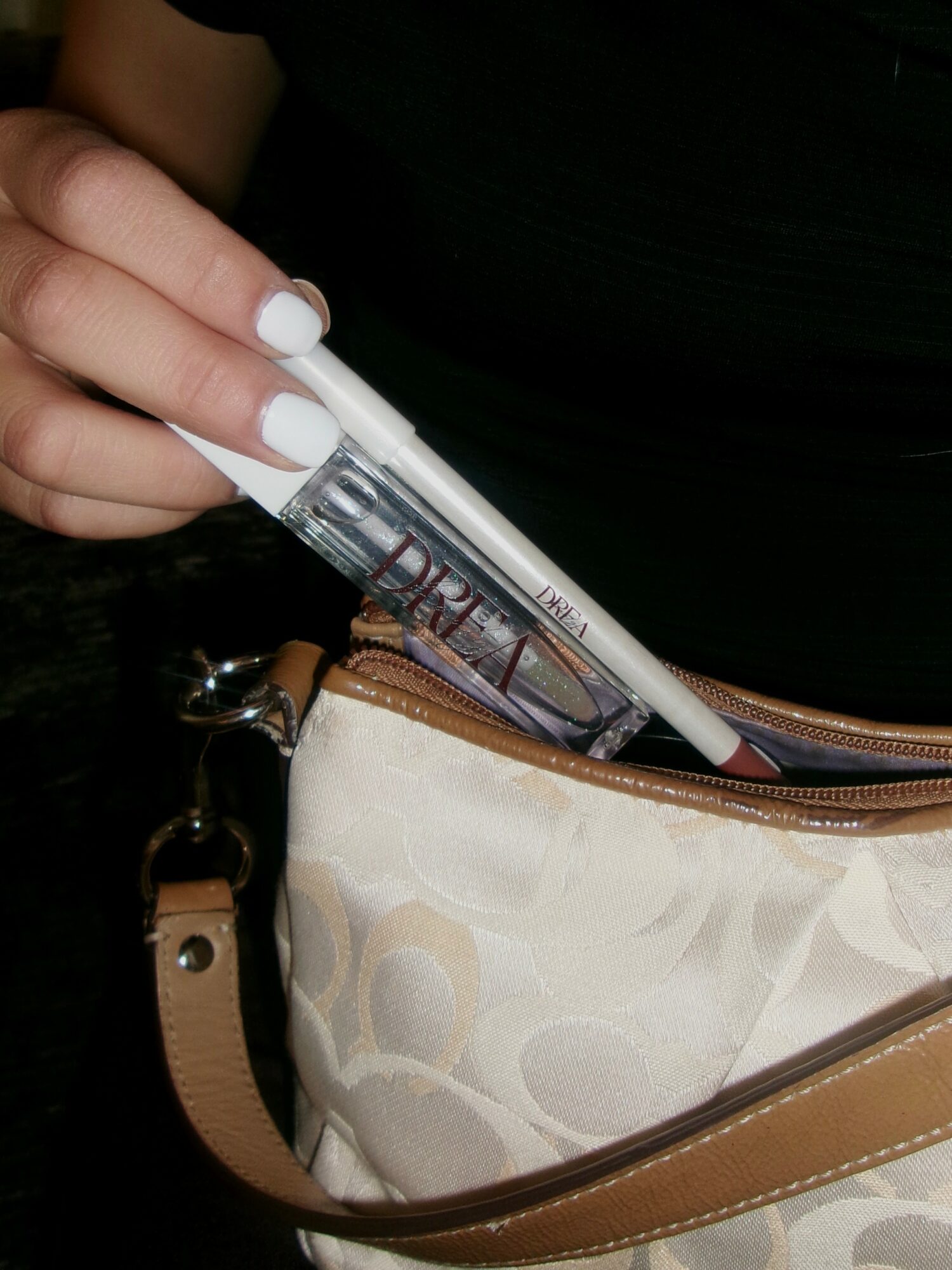 Person holding a test tube with a liquid, partially inside a beige and brown purse, against a dark background.