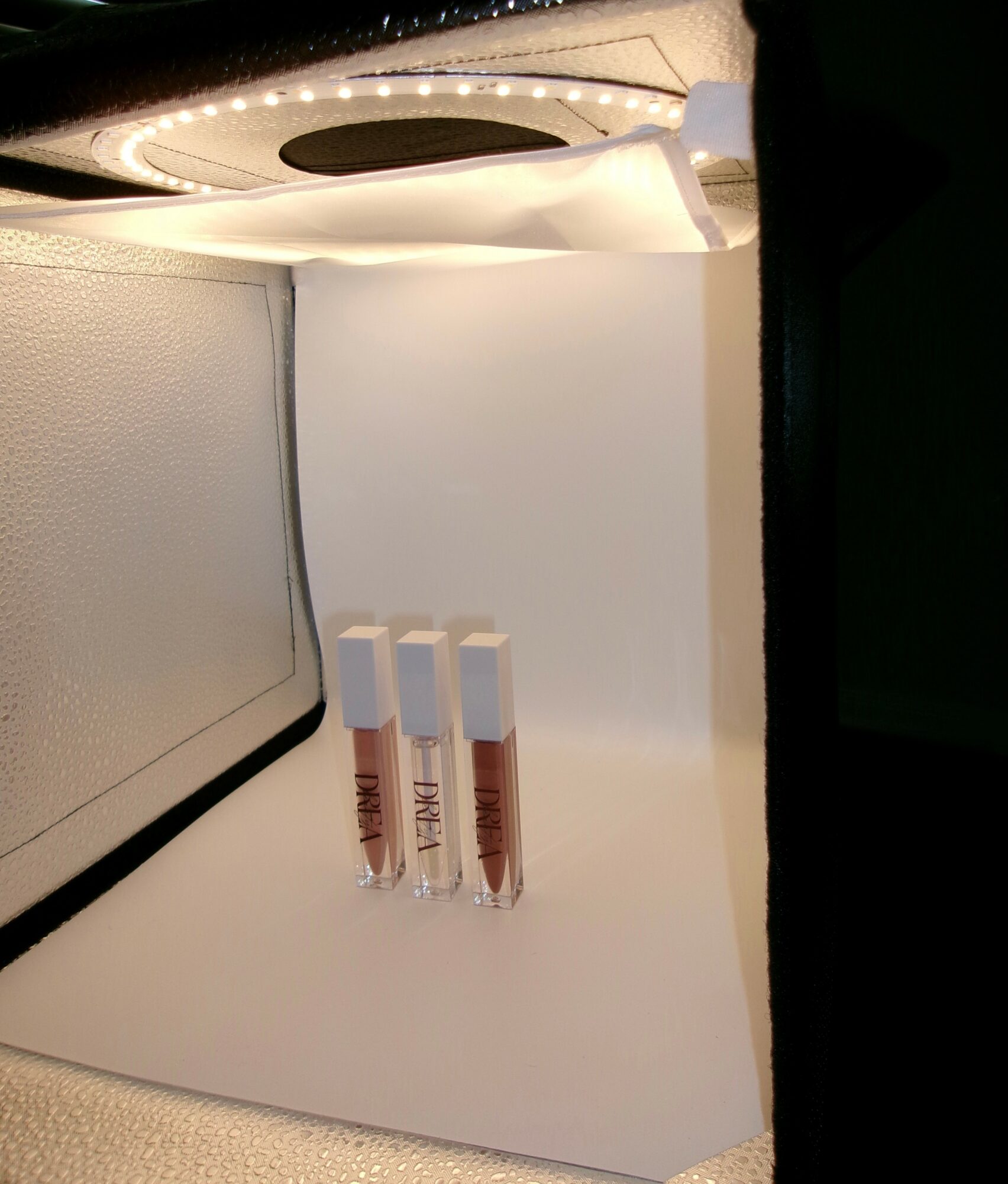 Three small vials with liquid inside are placed on a white surface, with a device and a wall in the background.