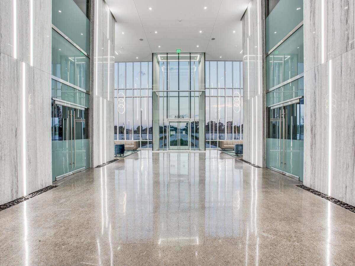 Modern building interior with glass walls, polished floor, and large windows showing cityscape outside.