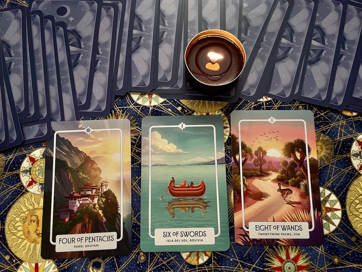 Three tarot cards laid out on a patterned surface with a candle above, depicting Four of Pentacles, Six of Swords, Eight of Wands.