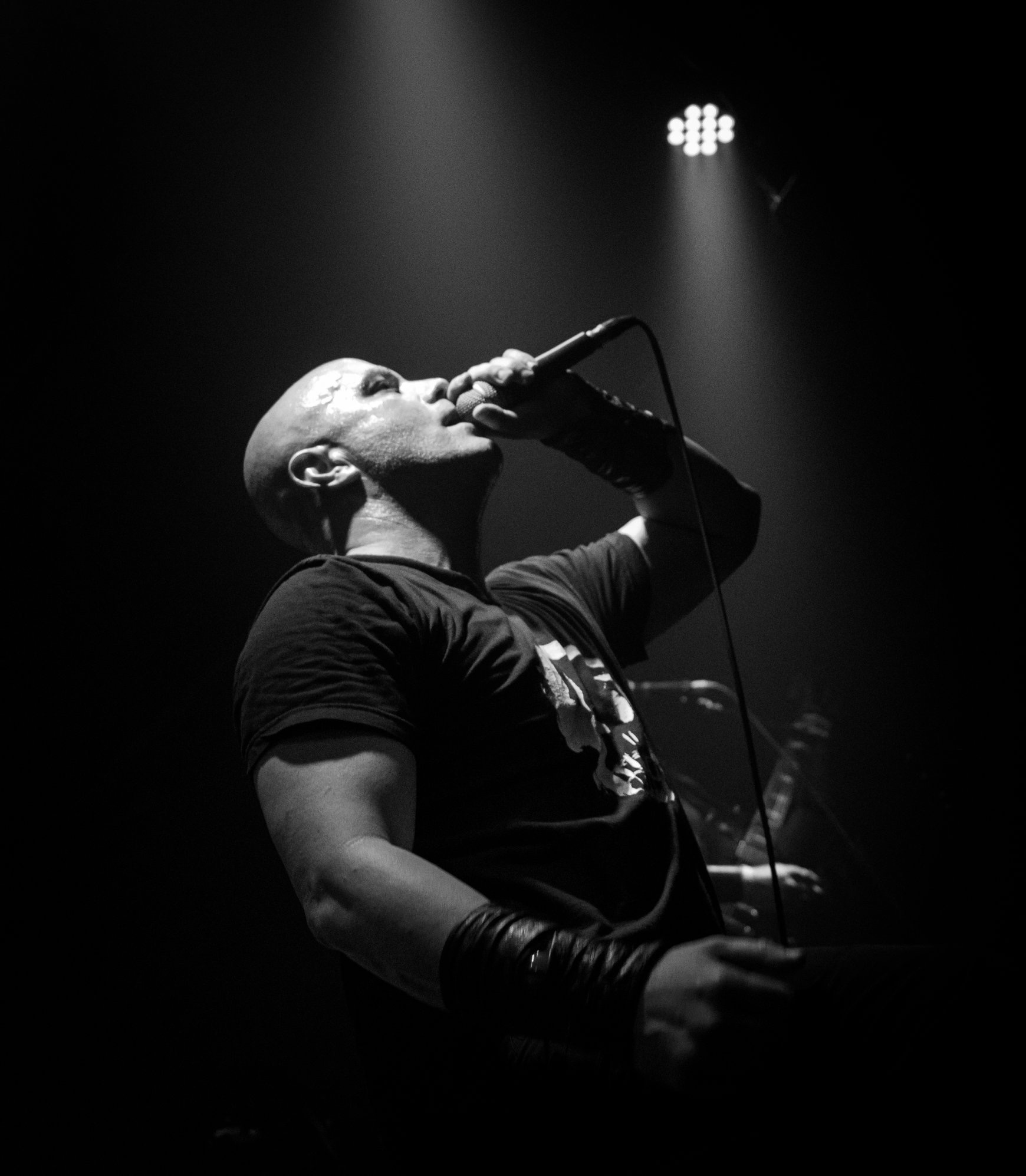 A person singing into a microphone on stage, illuminated by a spotlight, in black and white.