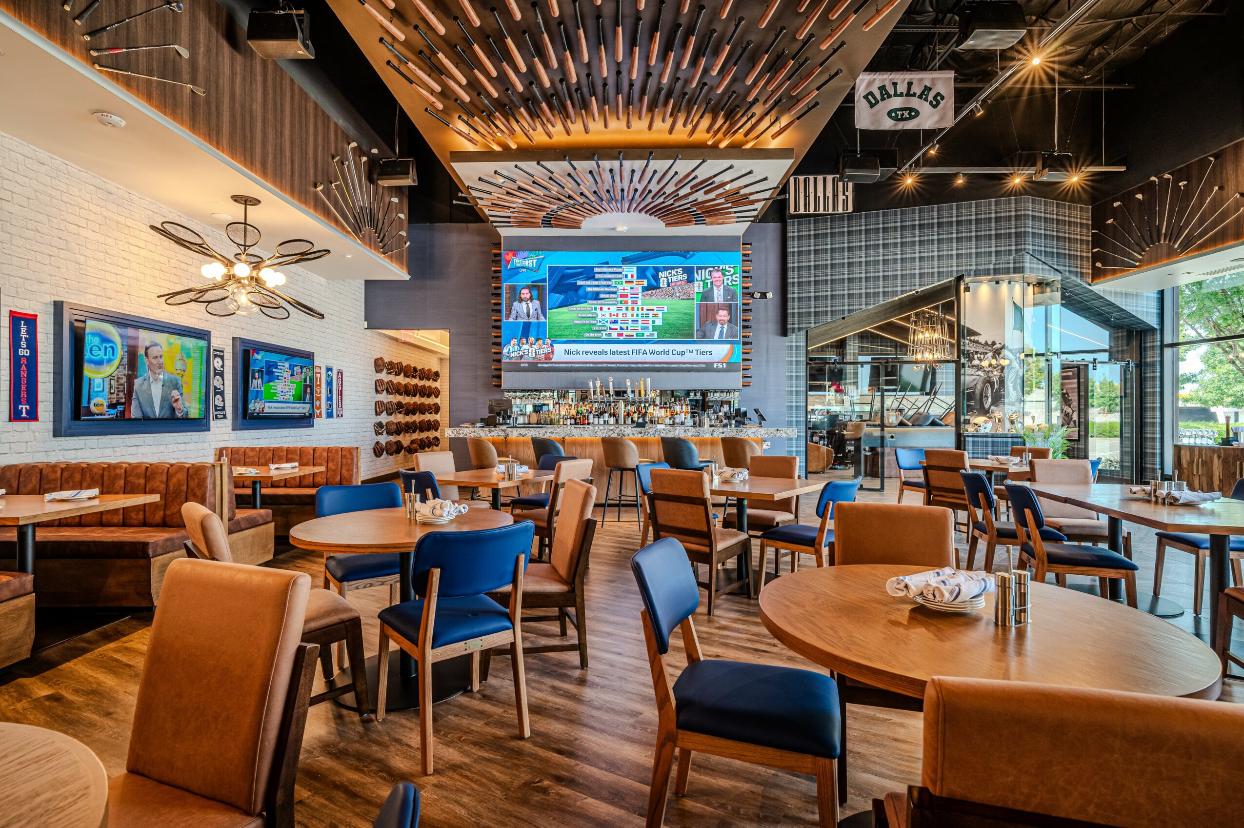 Restaurant interior with tables, chairs, large TV screens, and decorative ceiling elements, bright and modern atmosphere.