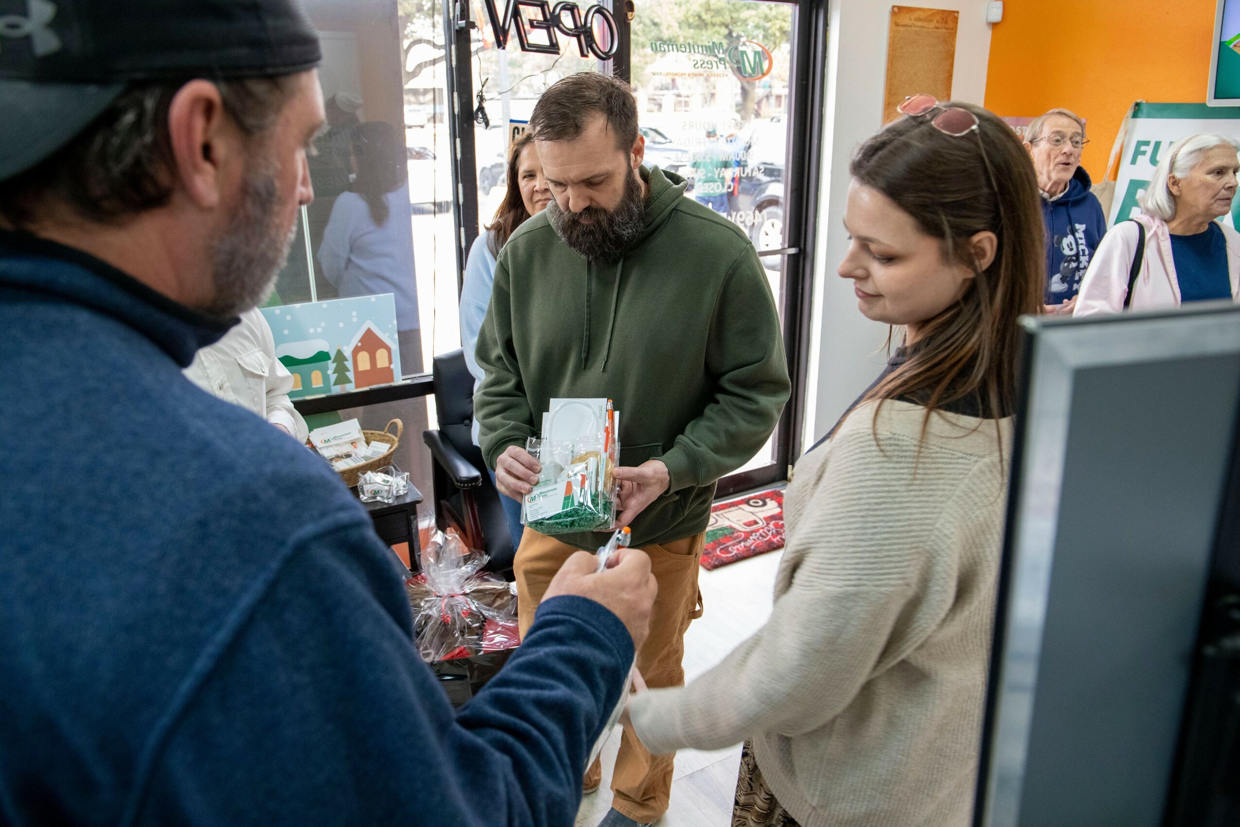People inside a store, with a man handing a card to a woman, and others in the background.
