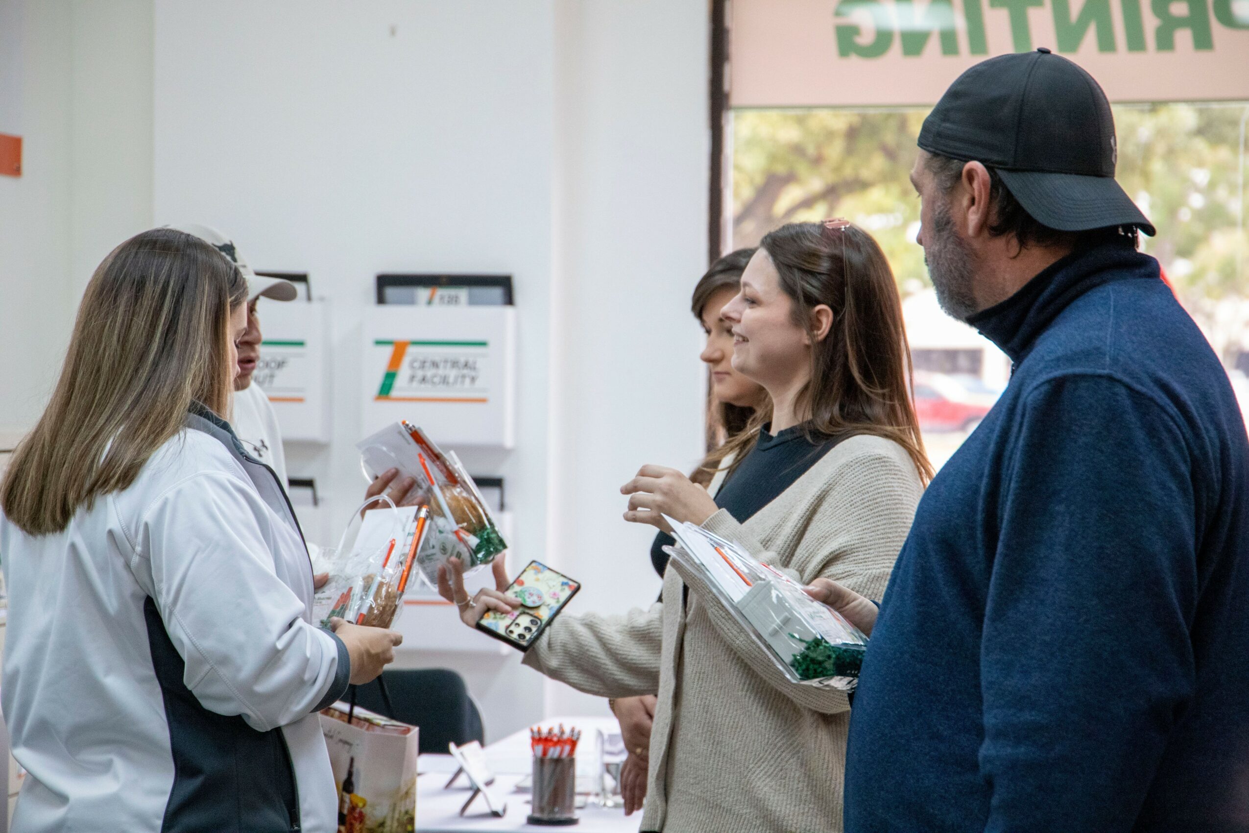 Group of four people talking inside a store, with a woman holding a brochure and others listening, near a window.