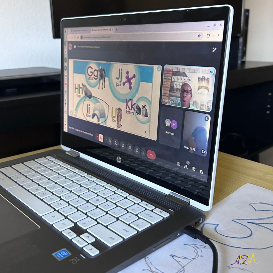 Laptop screen displaying a video call with multiple participants, a presentation slide, and a person wearing glasses. The laptop is on a desk with papers nearby.
