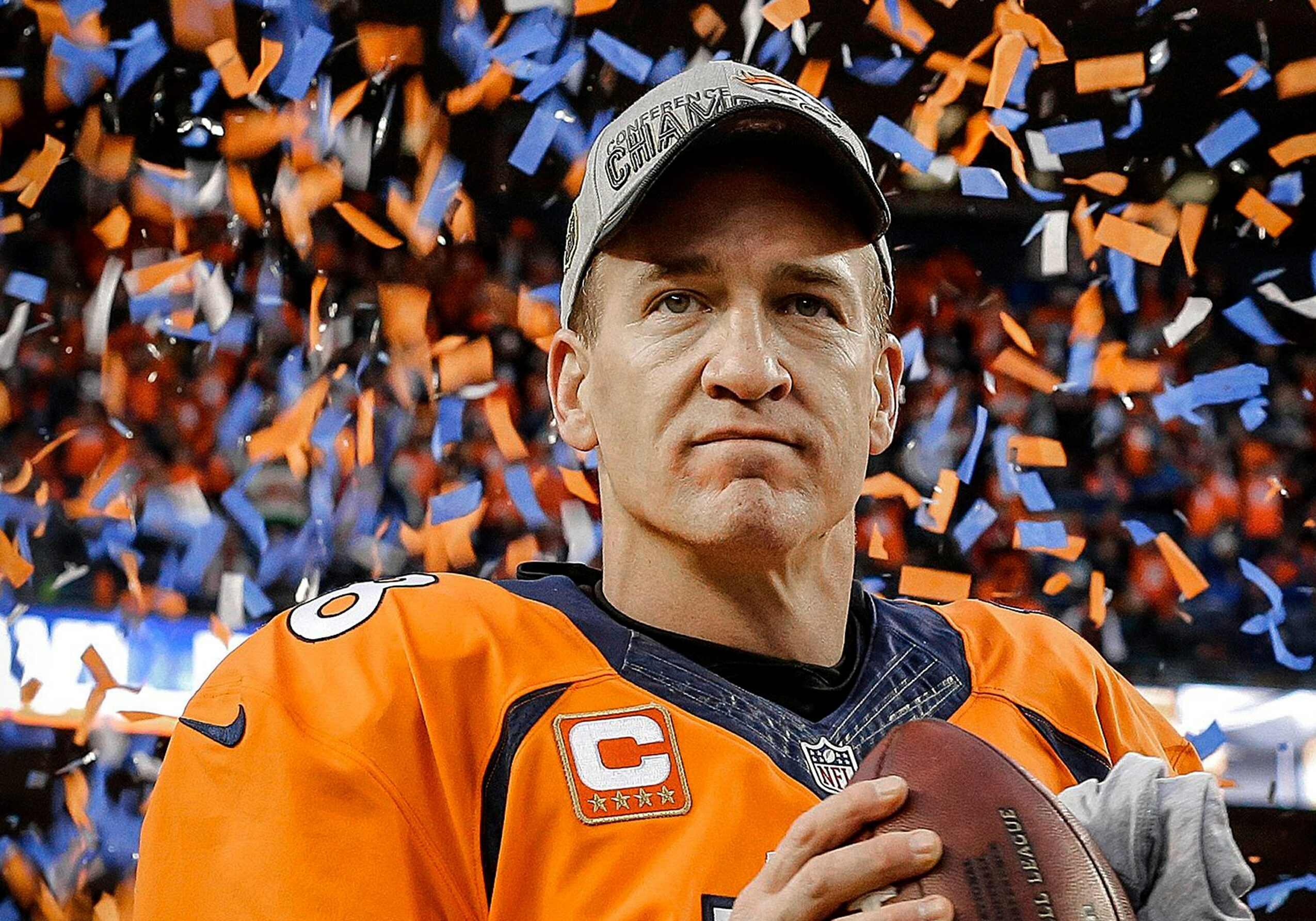 Male football player in orange jersey holding a football, with confetti falling in the background.